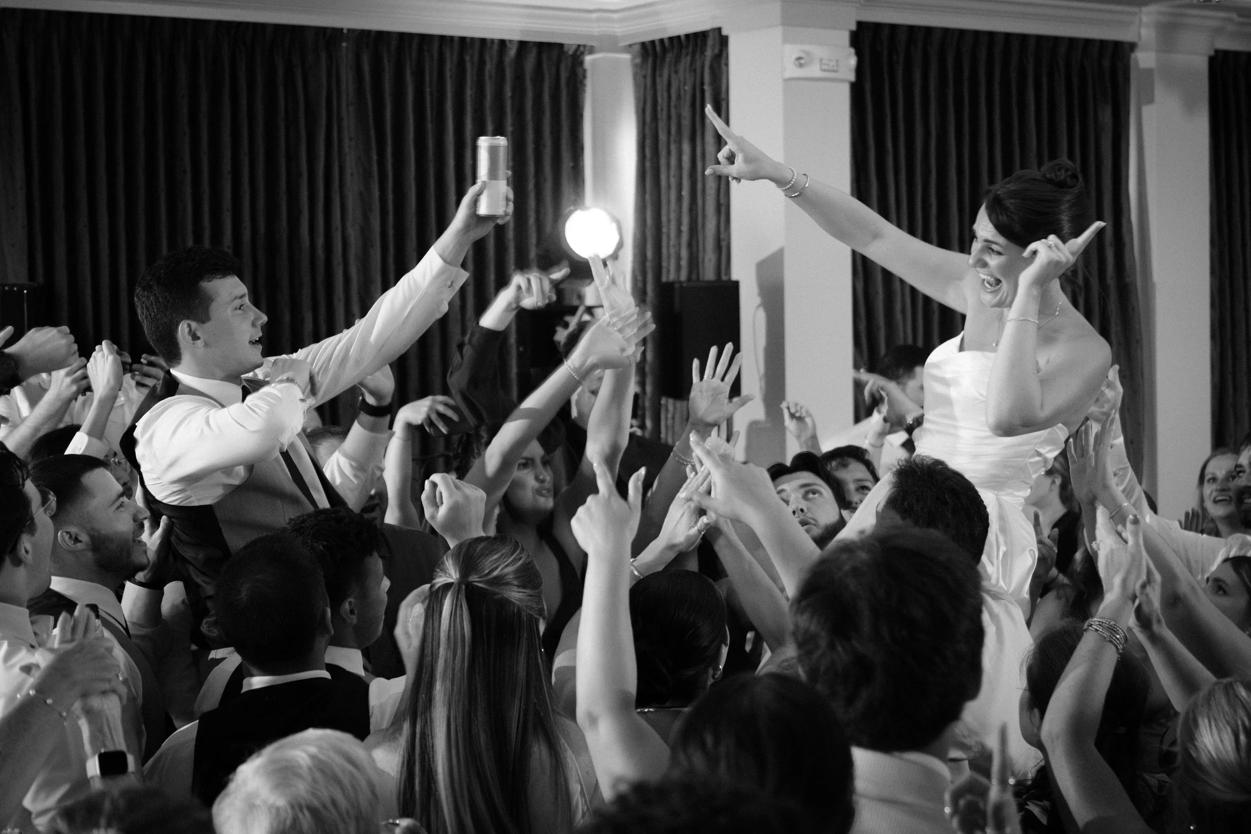 Caroline and Anthony Pirolli lifted on shoulders above the crowd with every hand in the air in black and white at Union Bluff Hotel in York Maine wedding photography VMG Productions