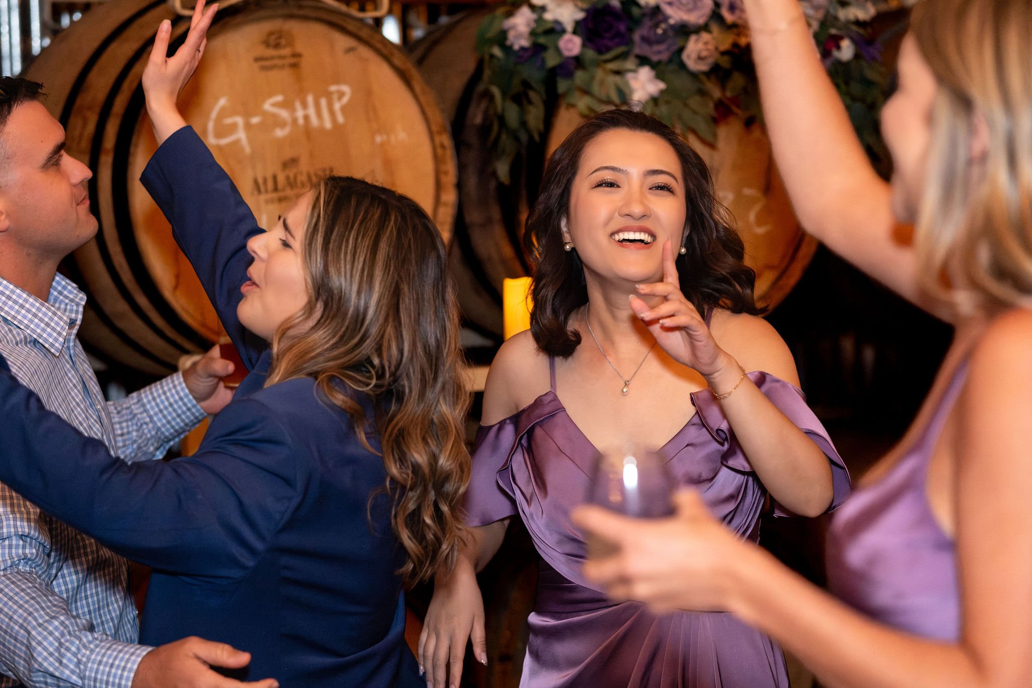 A bridesmaid in lavender laughing as she dances with friends in front of the barrels at The Cellars at Allagash Brewing Company in Portland Maine fall wedding photography VMG Productions
