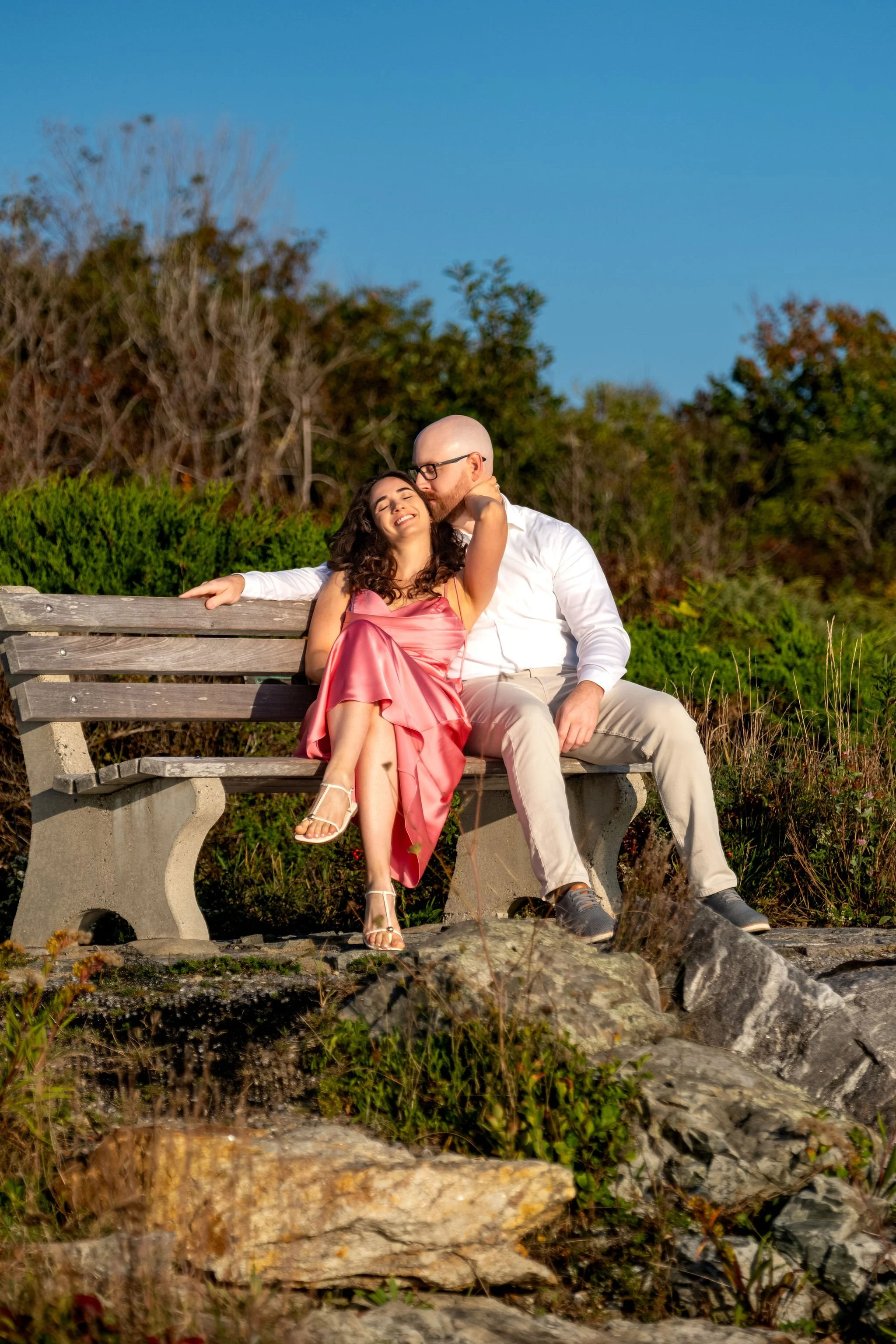 Helena resting her head against Zack as they cuddle on the bench on Marginal Way in Ogunquit Maine sunrise proposal and engagement photography VMG Productions