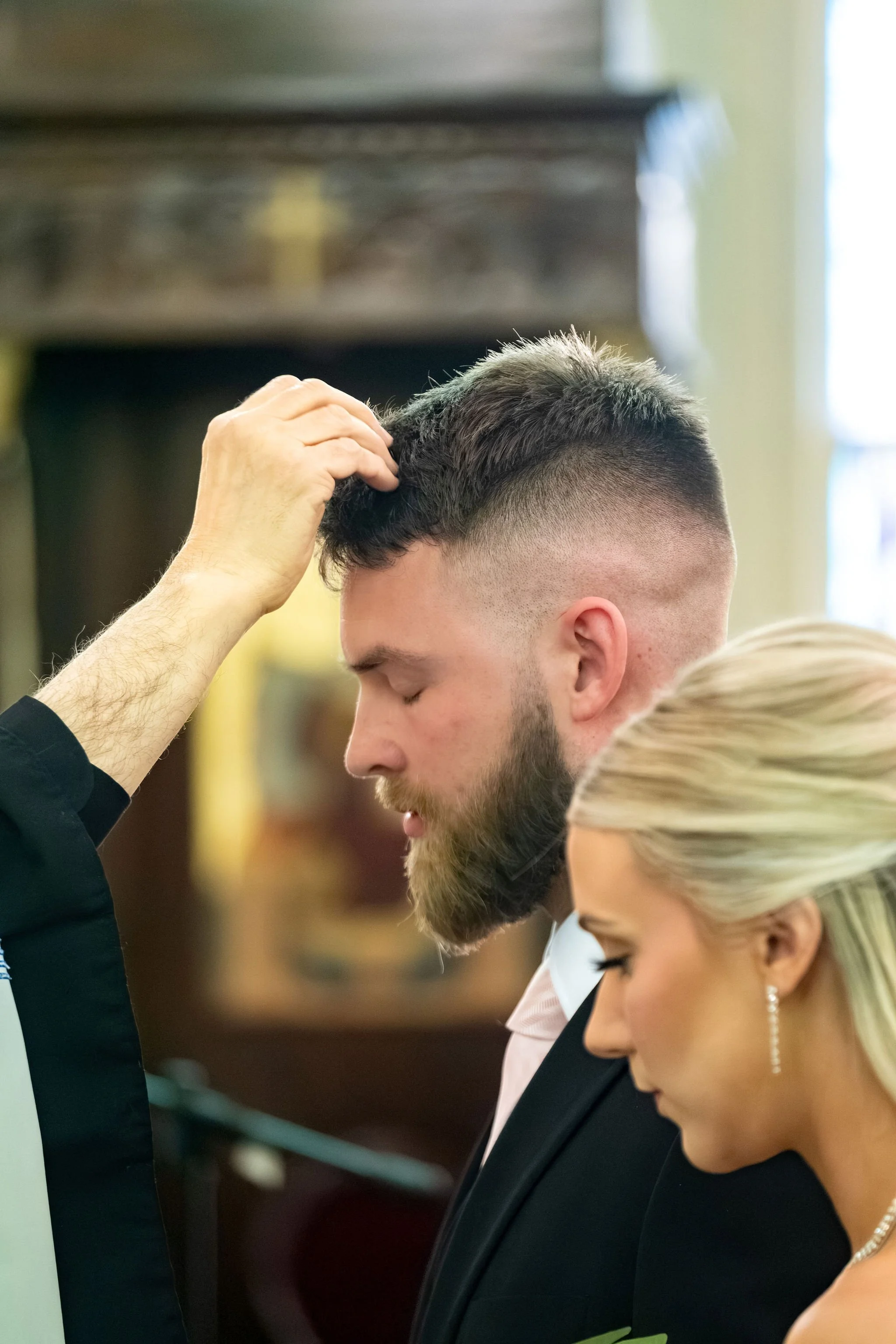 Jeremiah and Vienna priest performs a blessing while the couple bows their heads in prayer at Holy Trinity Greek Orthodox Church Portland Maine spring wedding photography VMG Productions