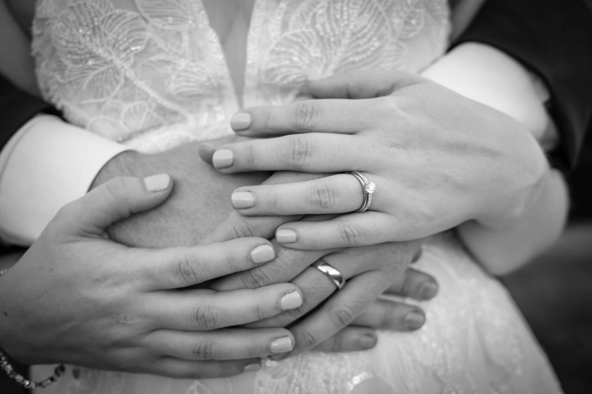 Black and white detail of Zachary and Hollie's hands and wedding rings clasped at her waist at The Lucerne Inn in Dedham Maine summer wedding photography VMG Productions