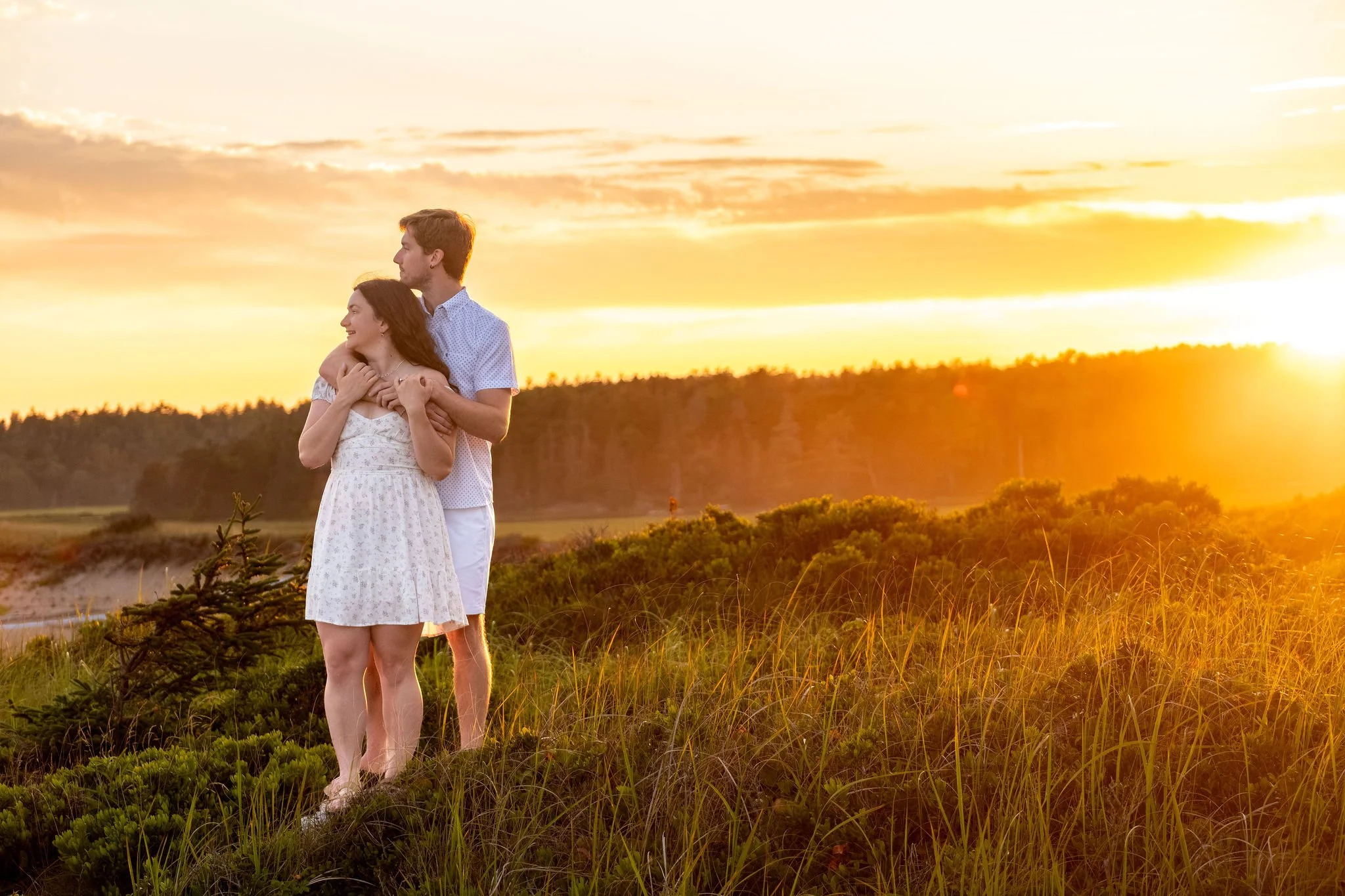 Kirstie and Lucas holding each other on the headland with the sun going down over the marsh at Reid State Park in Georgetown Maine engagement photography VMG Productions