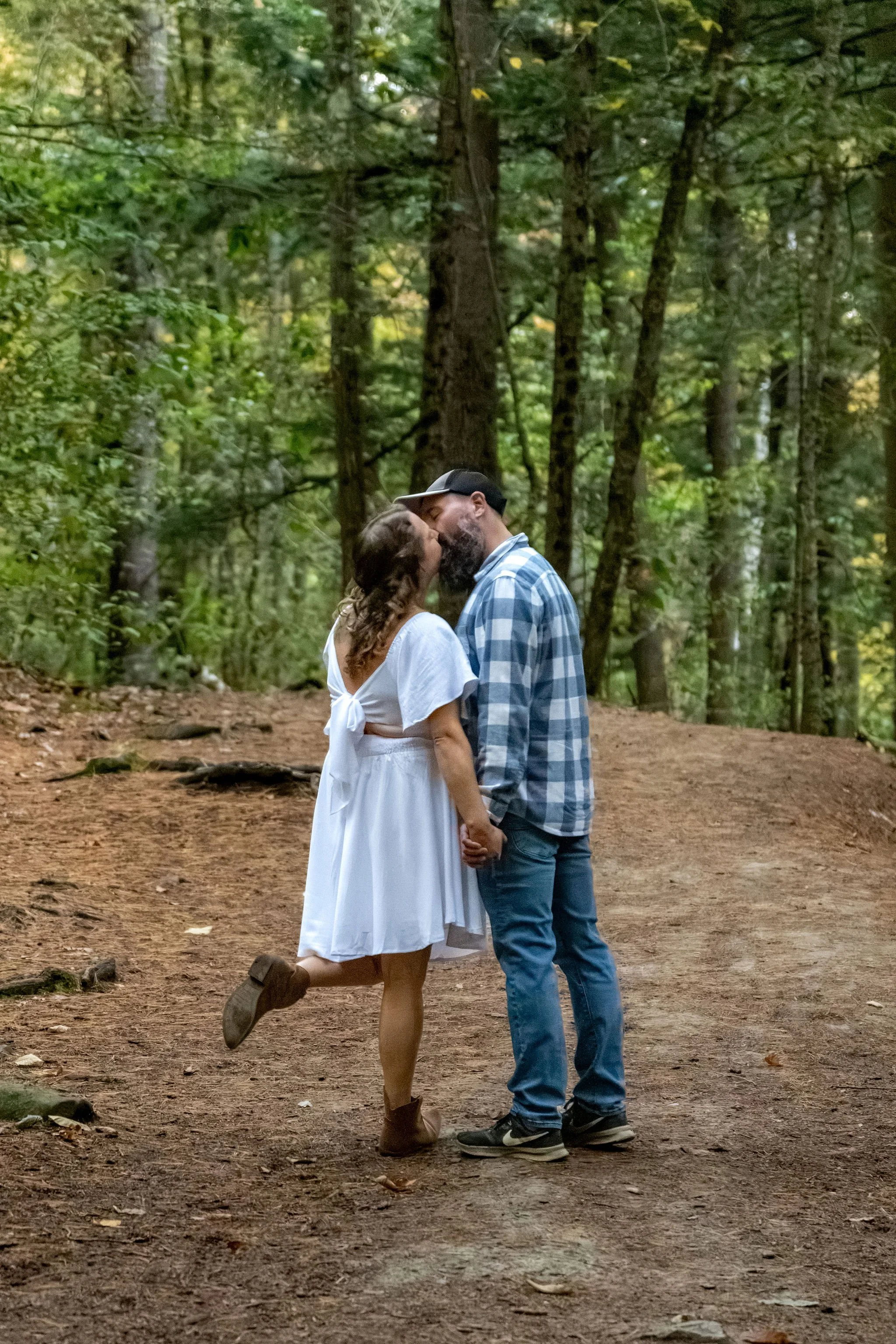 Alison popping her boot up as she kisses Dave on the trail at Vaughan Woods at Vaughan Woods in Hallowell Maine fall engagement photography VMG Productions