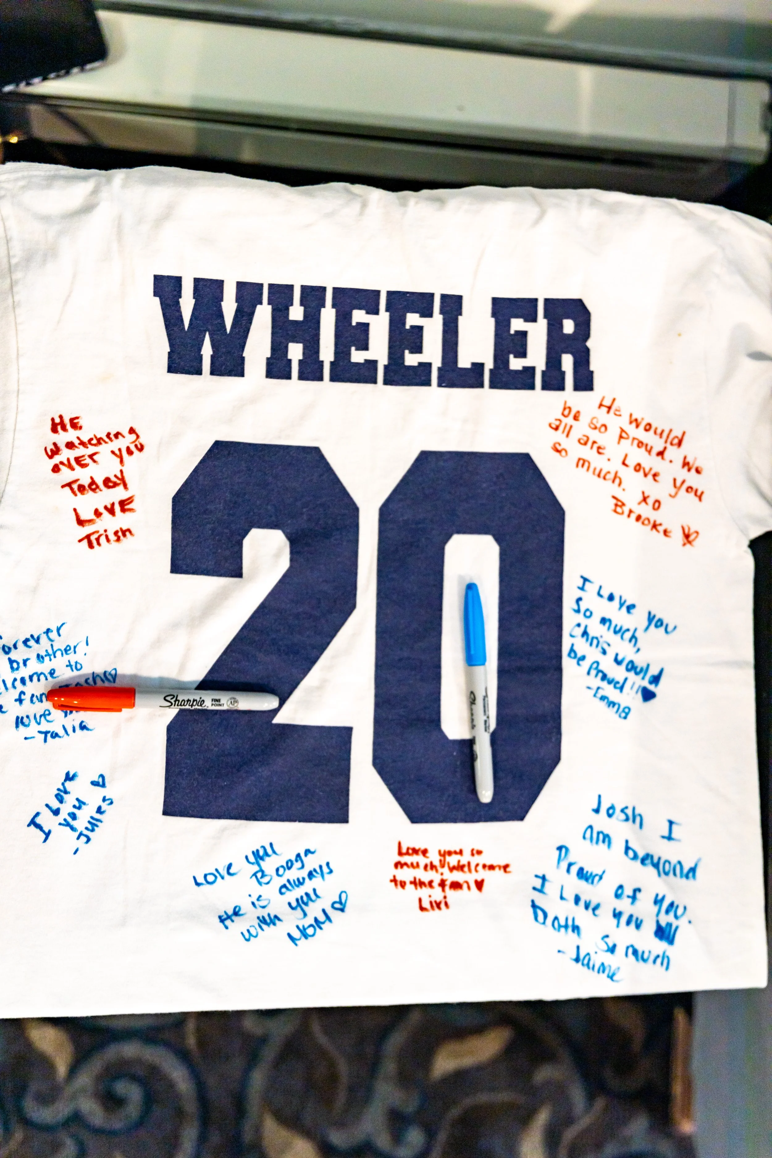 Sports jersey number 20 Wheeler covered in handwritten guest signatures and messages in blue and red Sharpie marker used as wedding guest book to be framed in shadow box at Black Swan Country Club Georgetown Massachusetts wedding 2021