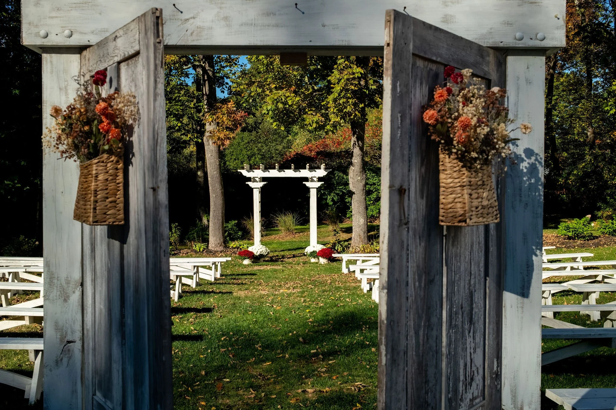 Weathered double doors with baskets of dried flowers opening onto the ceremony lawn and white pergola at Boothbay Playhouse in Boothbay Maine fall wedding photography VMG Productions