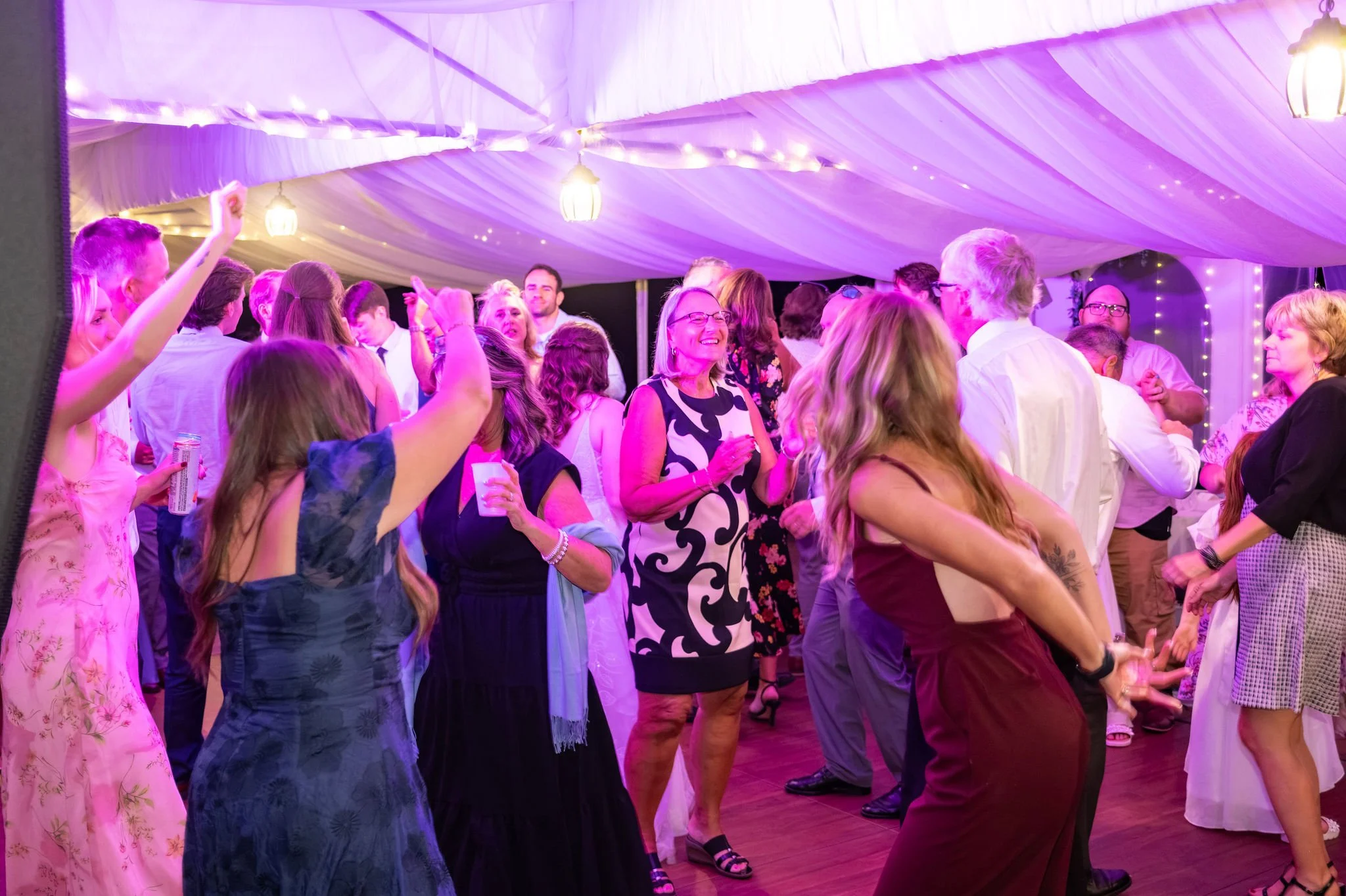 Guests packed onto the dance floor under the tent lit in blue and pink at The Lucerne Inn in Dedham Maine summer wedding photography VMG Productions