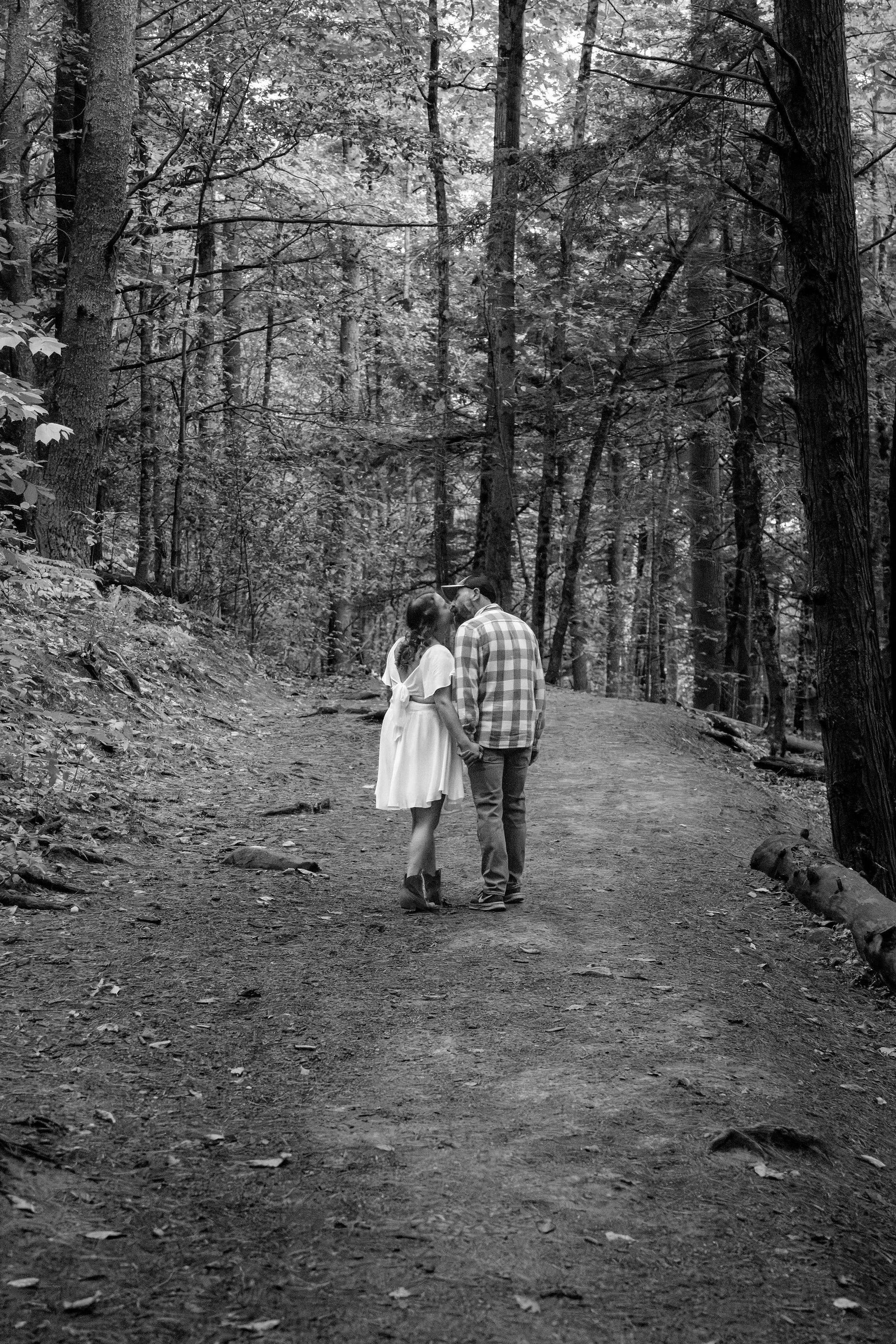 Black and white of Alison and Dave walking close together up the trail at Vaughan Woods in Hallowell Maine fall engagement photography VMG Productions