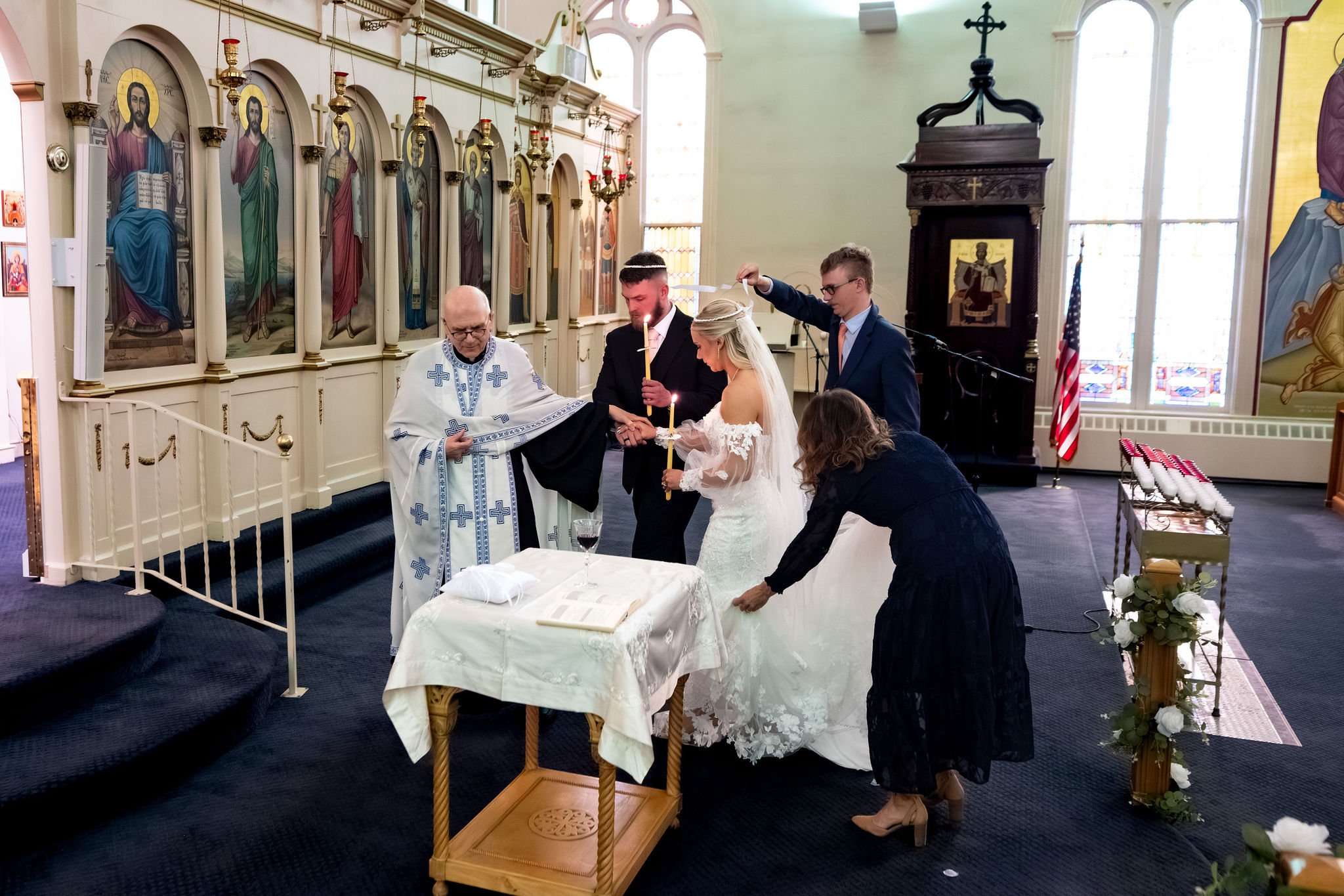 Jeremiah and Vienna participate in a ceremonial Orthodox wedding tradition assisted by family and attendants at Holy Trinity Greek Orthodox Church Portland Maine spring wedding photography VMG Productions