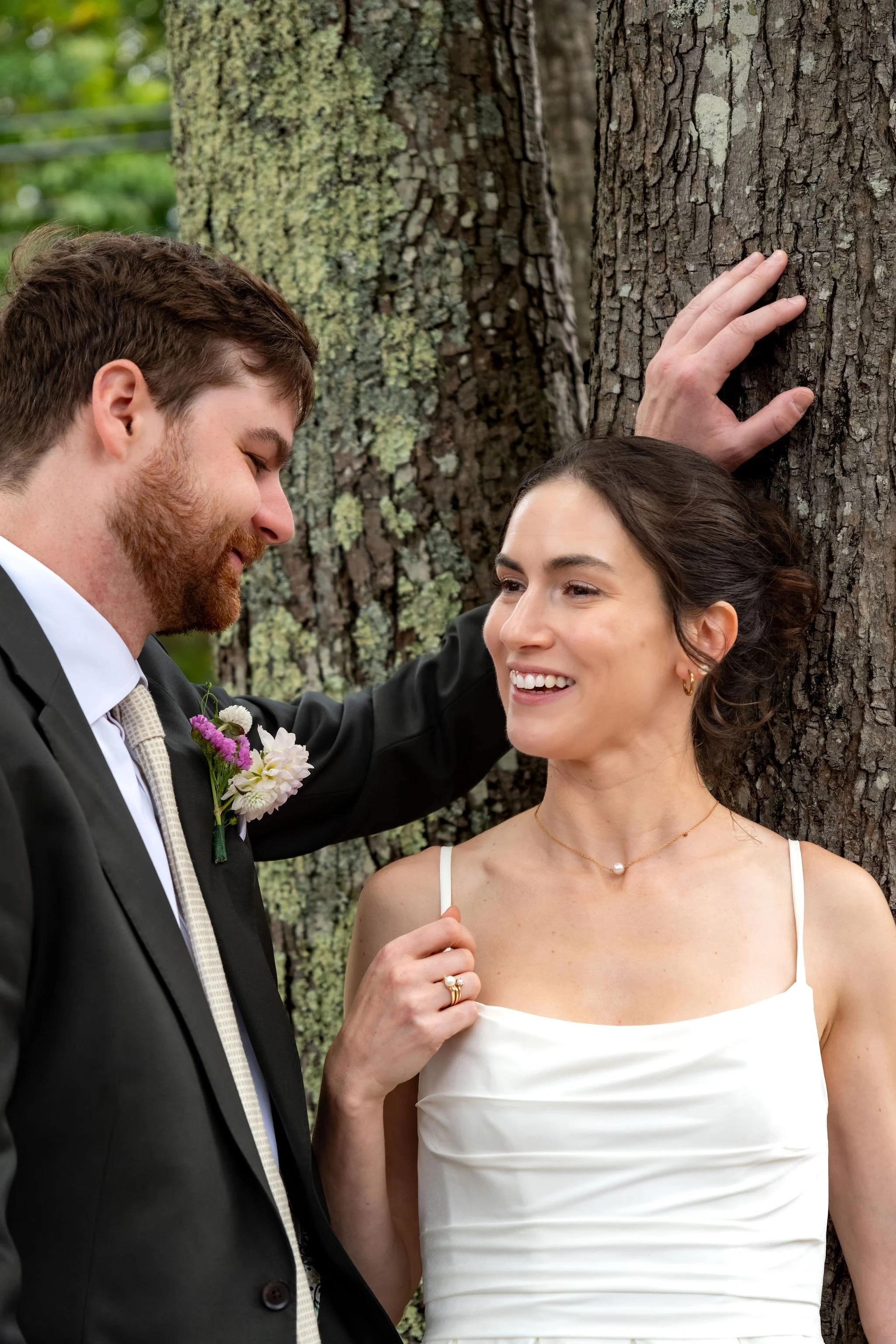 Victoria smiling as Jack leans in beside her against the tree trunk at The Cellars at Allagash Brewing Company in Portland Maine fall wedding photography VMG Productions