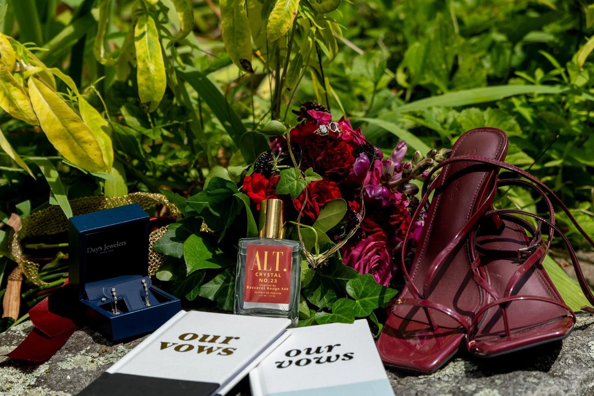 Cassidy Begin's burgundy heels vow books perfume and earrings styled on a stone wall at Maple Hill Farm Inn and Conference Center in Hallowell Maine summer wedding photography VMG Productions