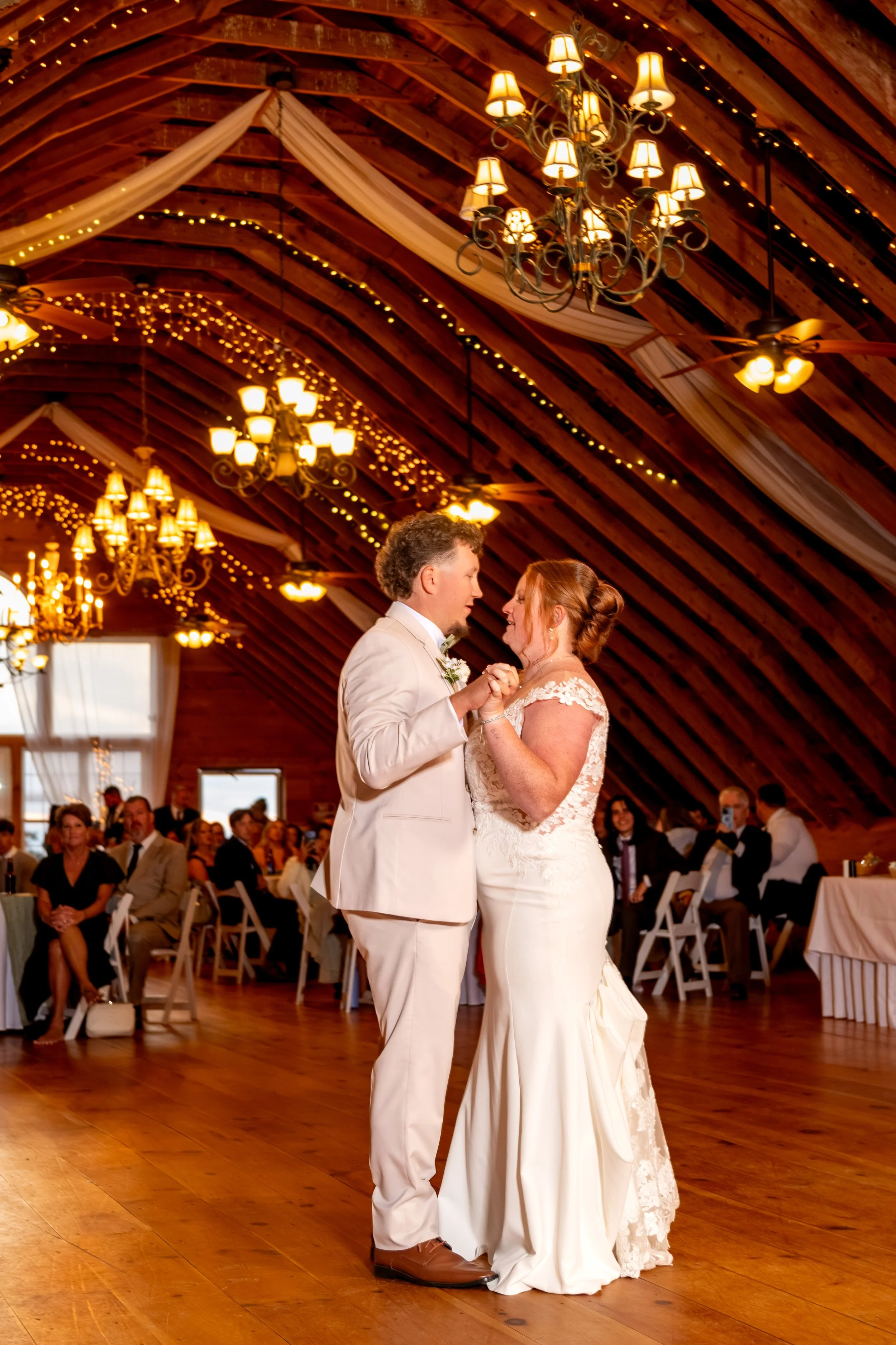 Andrew and Erika slow dancing under the barn's chandeliers and string lights at the Maine Wedding Barn and Event Center in Minot Maine fall wedding photography VMG Productions