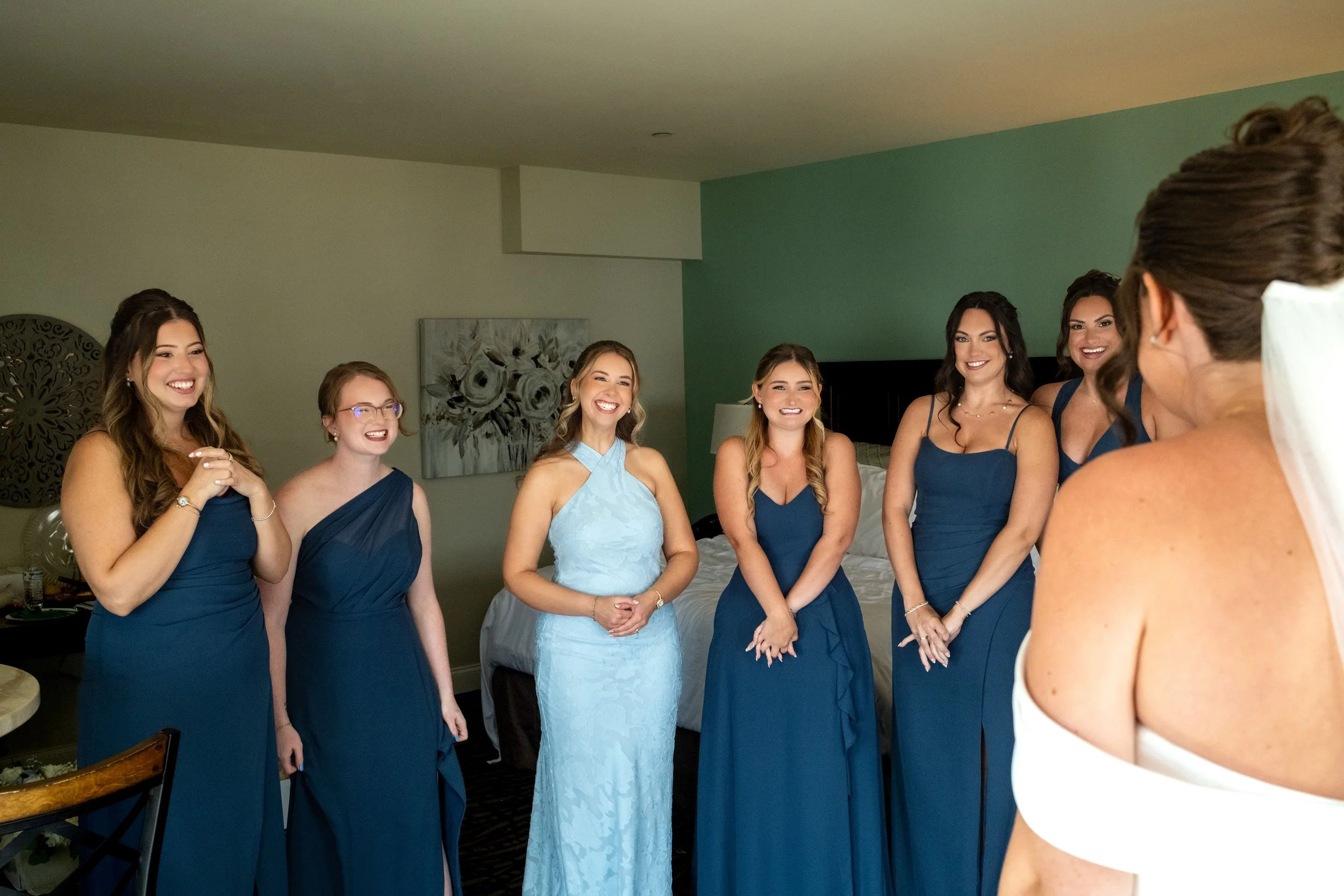 Caroline Pirolli's bridesmaids in navy smiling as they see her in her gown for the first time in the bridal suite at Union Bluff Hotel in York Maine wedding photography VMG Productions