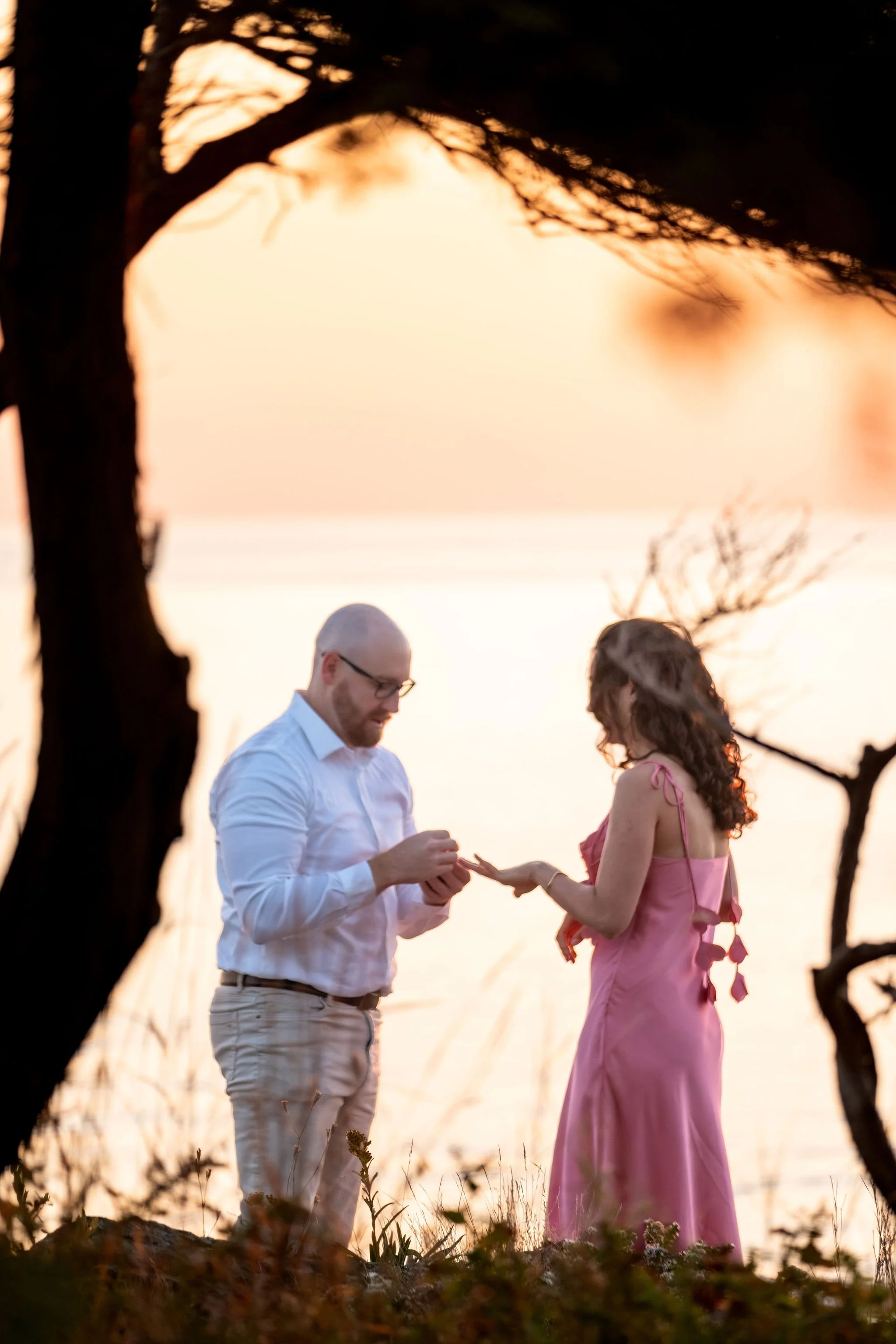 Helena holding out her hand as Zack finishes placing the ring on her finger on Marginal Way in Ogunquit Maine sunrise proposal and engagement photography VMG Productions