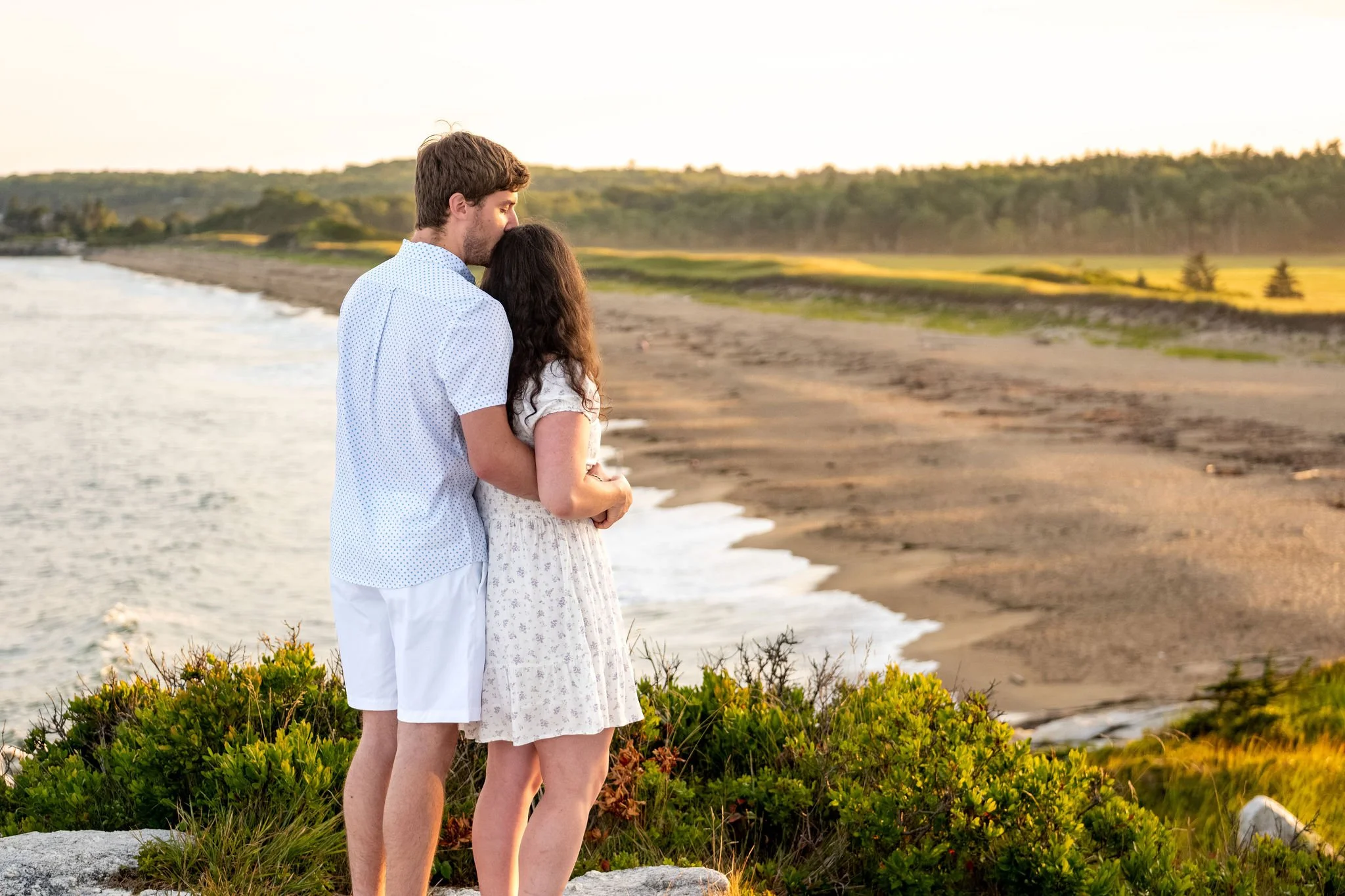Kirstie and Lucas looking out over the long curve of beach and surf from the headland at Reid State Park in Georgetown Maine engagement photography VMG Productions
