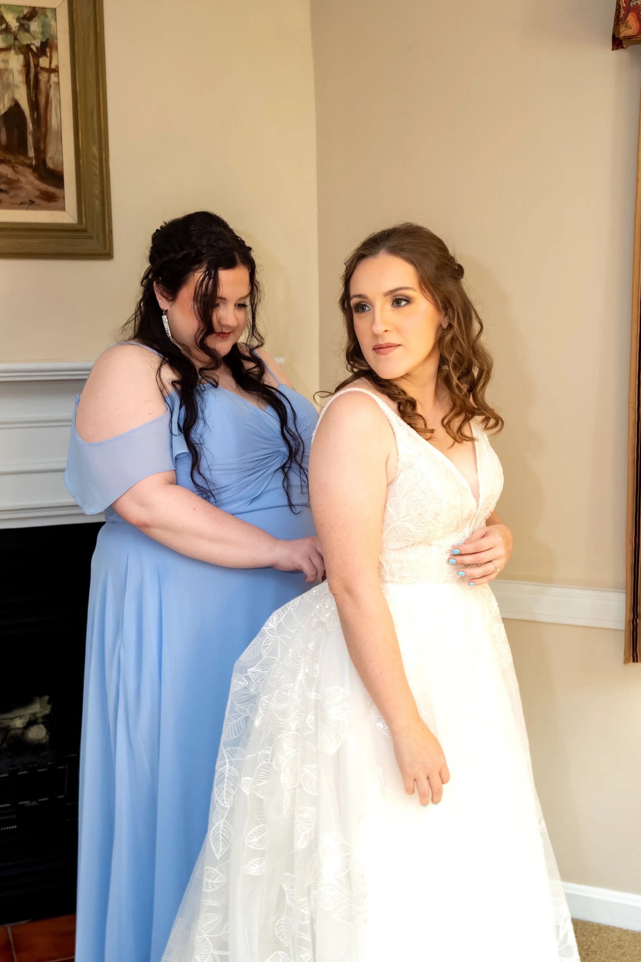 Hollie in her gown with a bridesmaid in dusty blue beside her in the getting ready room at The Lucerne Inn in Dedham Maine summer wedding photography VMG Productions