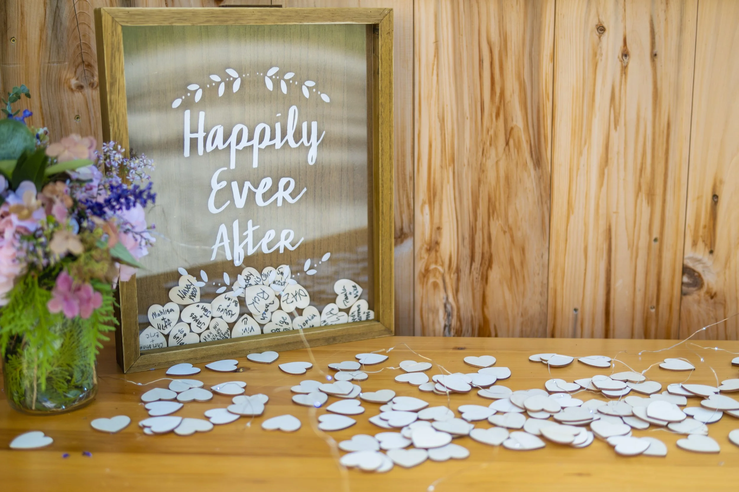 Shadow box drop frame wedding guest book reading Happily Ever After with wooden heart tokens and wildflower arrangement on barn wood table at Harvest Moon Farm Winthrop Maine wedding