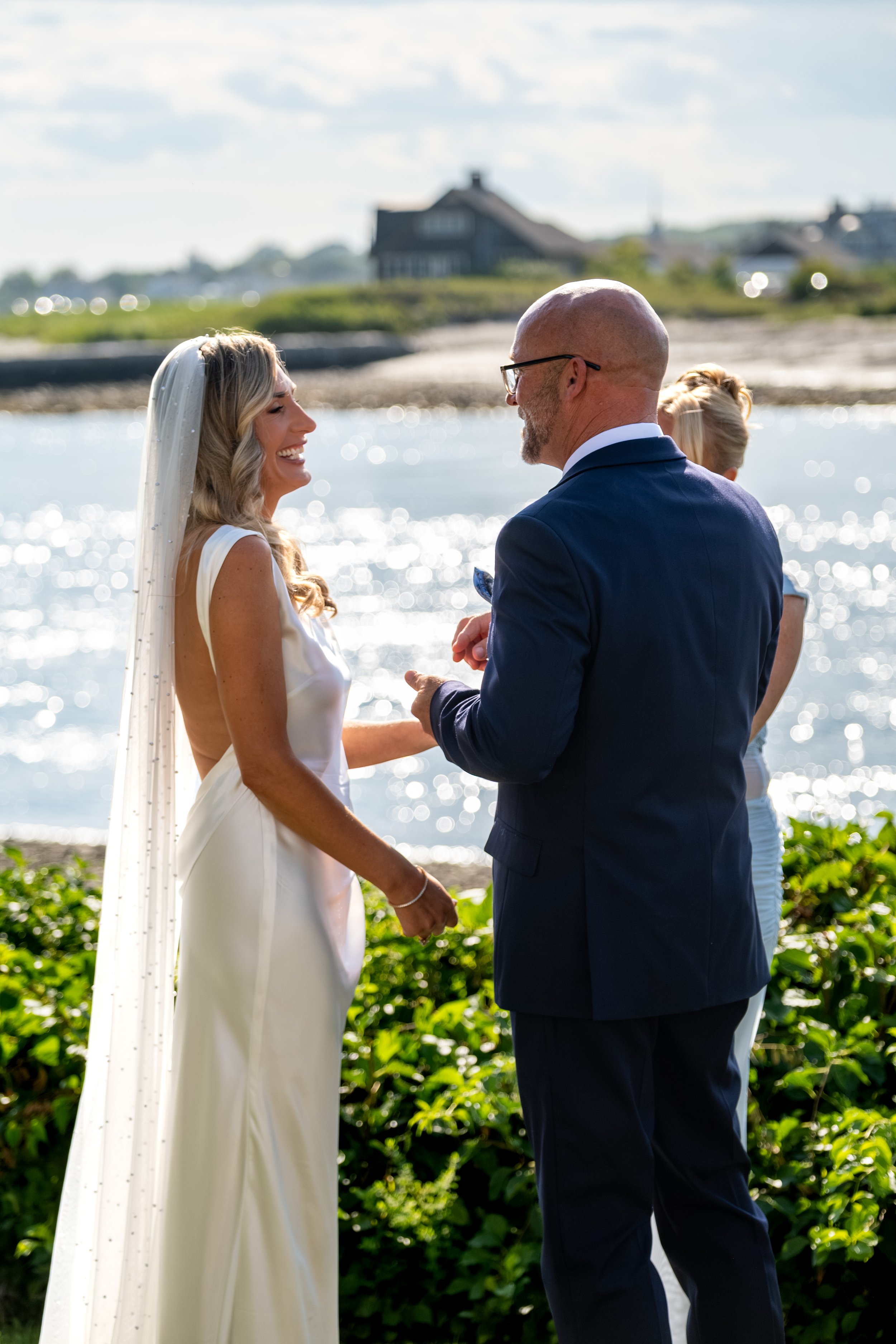 Ashley Draper laughing during the vows as Marc's sister Bonnie officiates on the waterfront lawn at The Breakwater Inn in Kennebunkport Maine summer wedding photography VMG Productions
