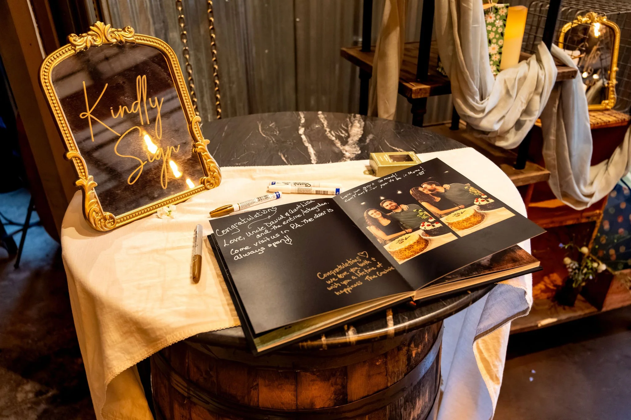 Gold mirror guest book sign reading Kindly Sign beside an open photo guest book on a barrel table at The Cellars at Allagash Brewing Company in Portland Maine fall wedding photography VMG Productions