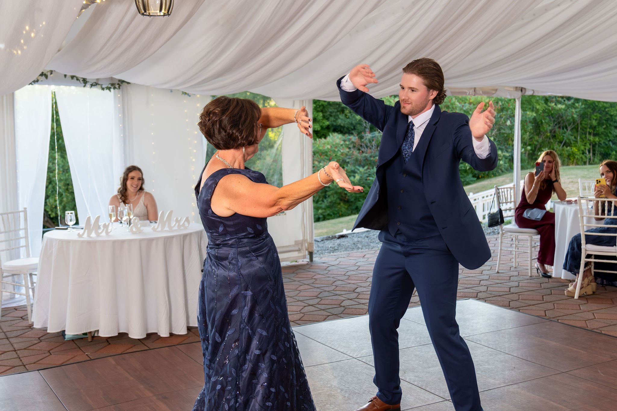 Zachary and his mom dancing with their arms up on the dance floor as guests laugh at The Lucerne Inn in Dedham Maine summer wedding photography VMG Productions