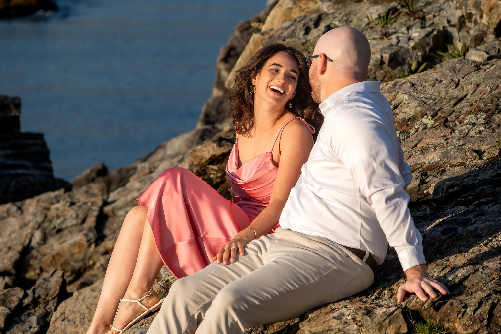 Helena laughing with her head tipped back as Zack leans in beside her on the rocks on Marginal Way in Ogunquit Maine sunrise proposal and engagement photography VMG Productions