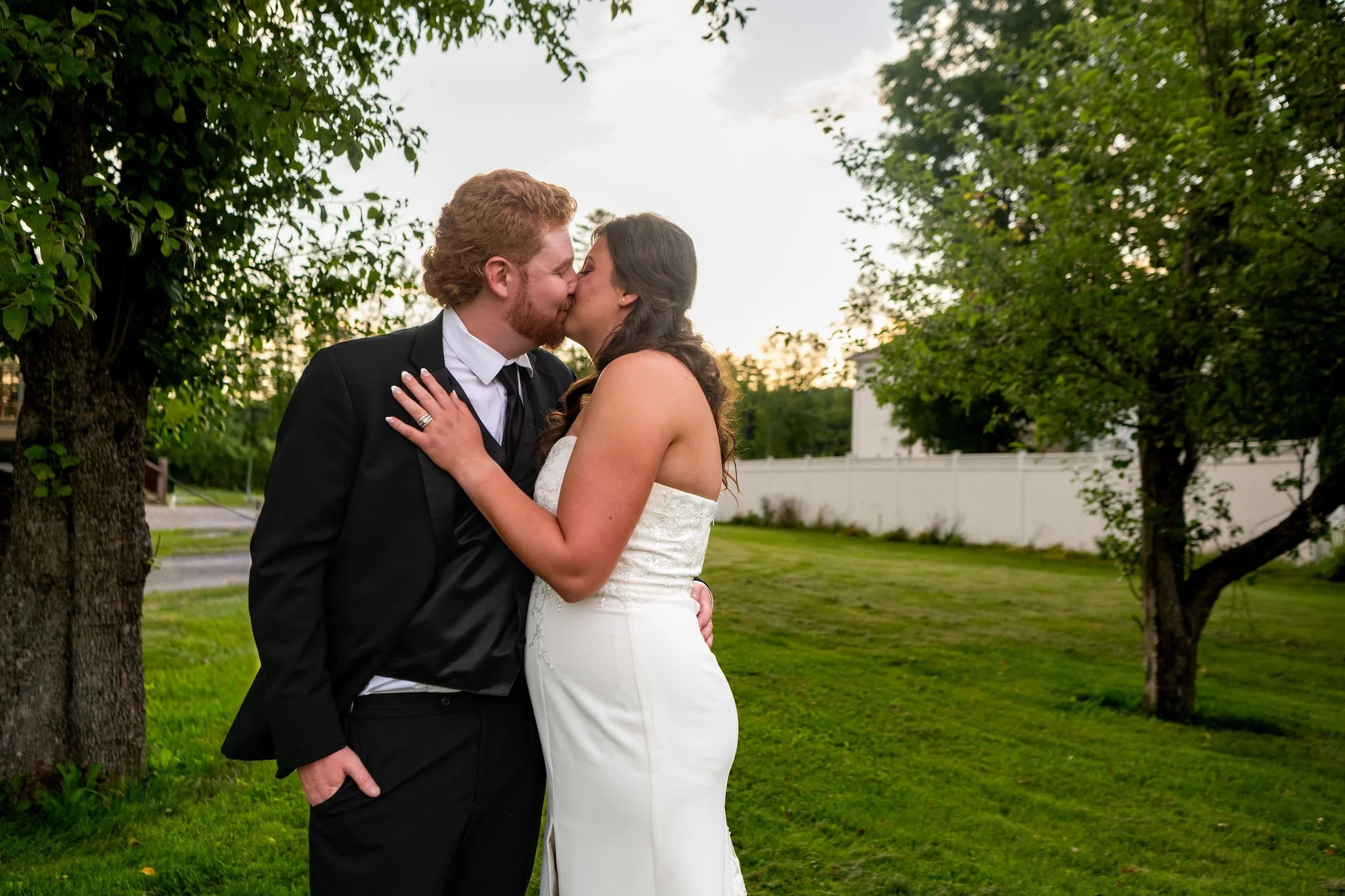 Alyssa and Colby kissing at golden hour on the lawn outside the 1888 Barn Bethel Maine summer wedding photography VMG Productions