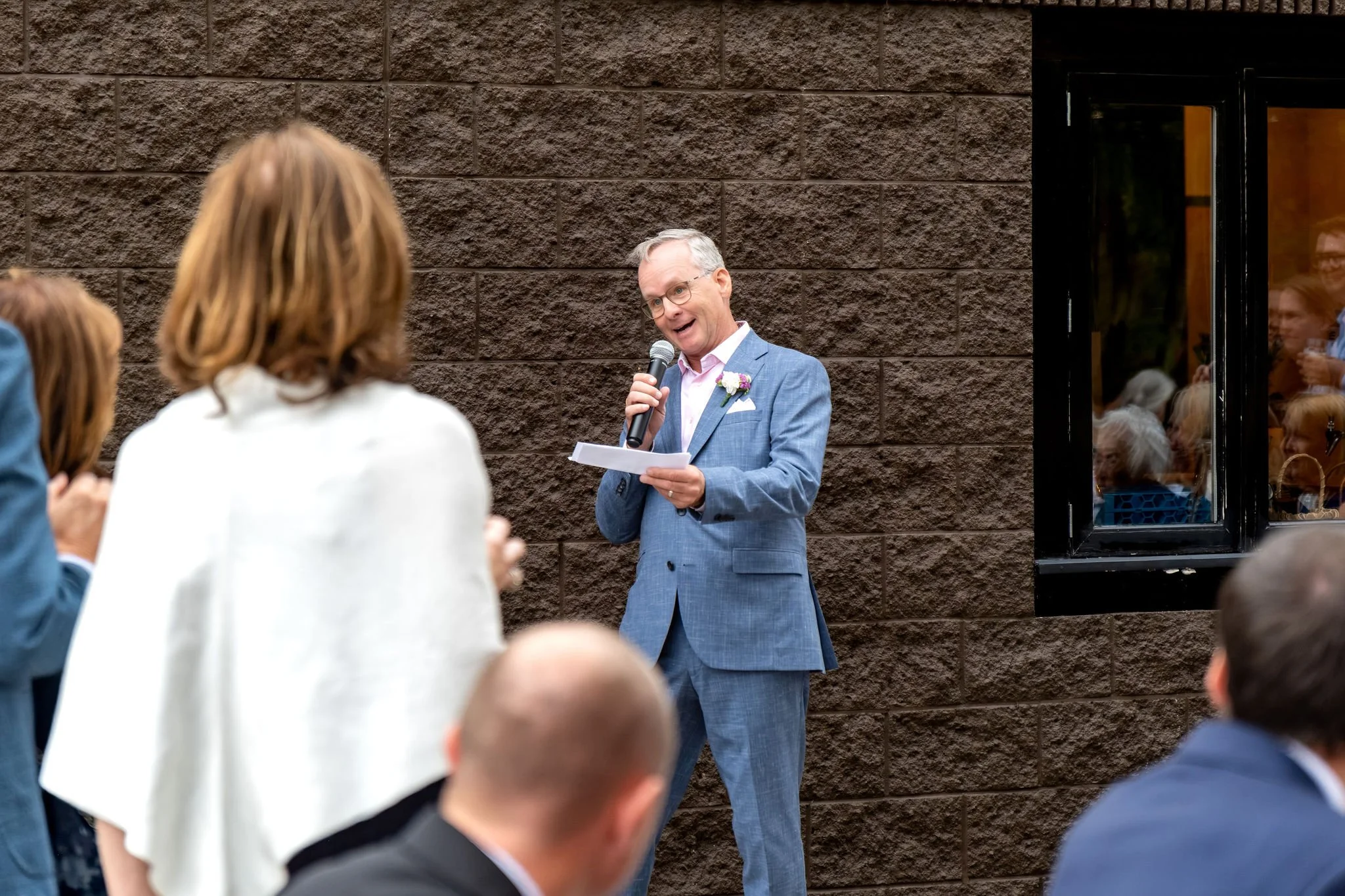 Jack's dad reading his toast into a microphone on the patio at The Cellars at Allagash Brewing Company in Portland Maine fall wedding photography VMG Productions