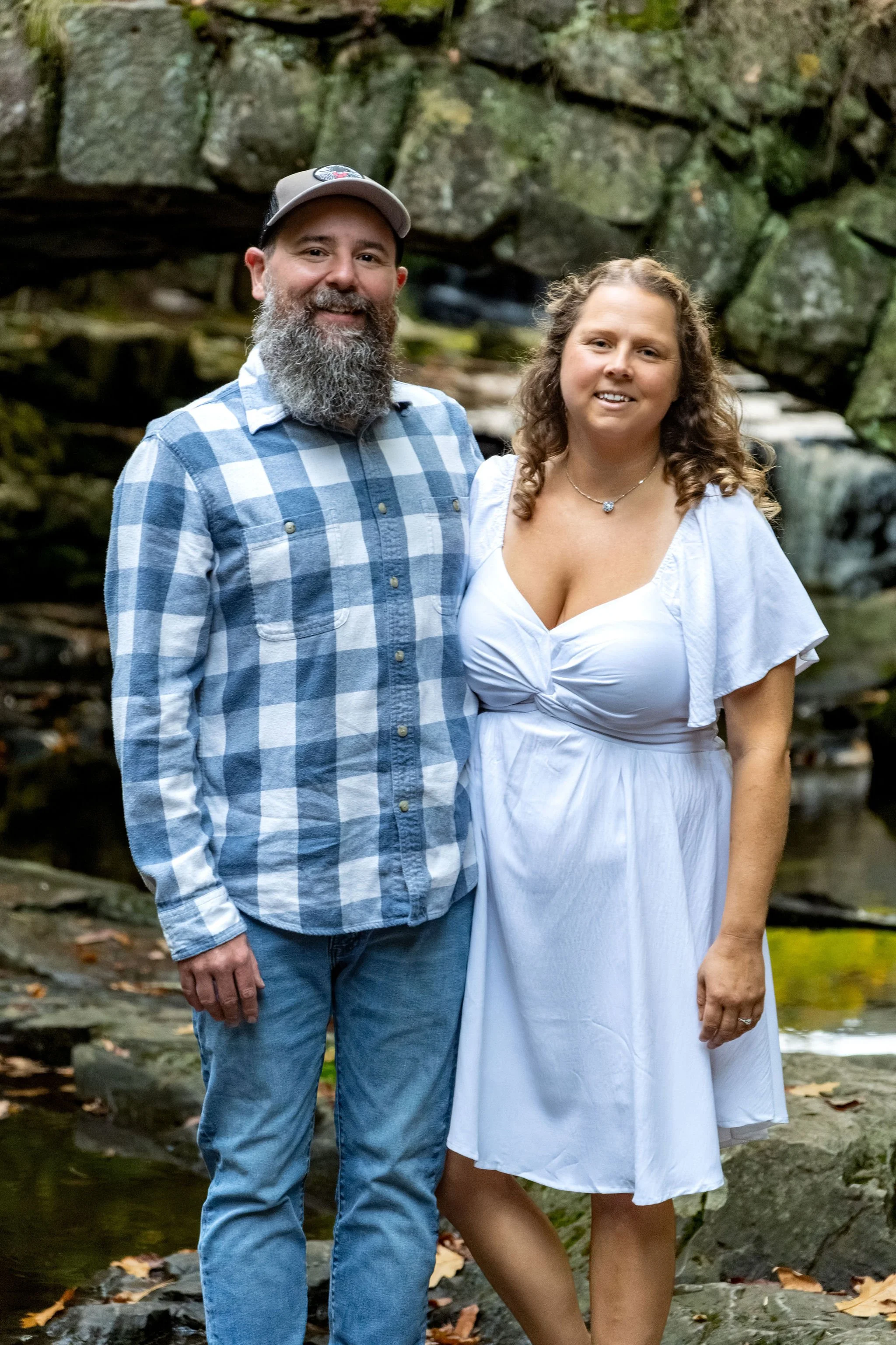 Close portrait of Alison and Dave smiling under the stone arch with the waterfall behind them at Vaughan Woods in Hallowell Maine fall engagement photography VMG Productions
