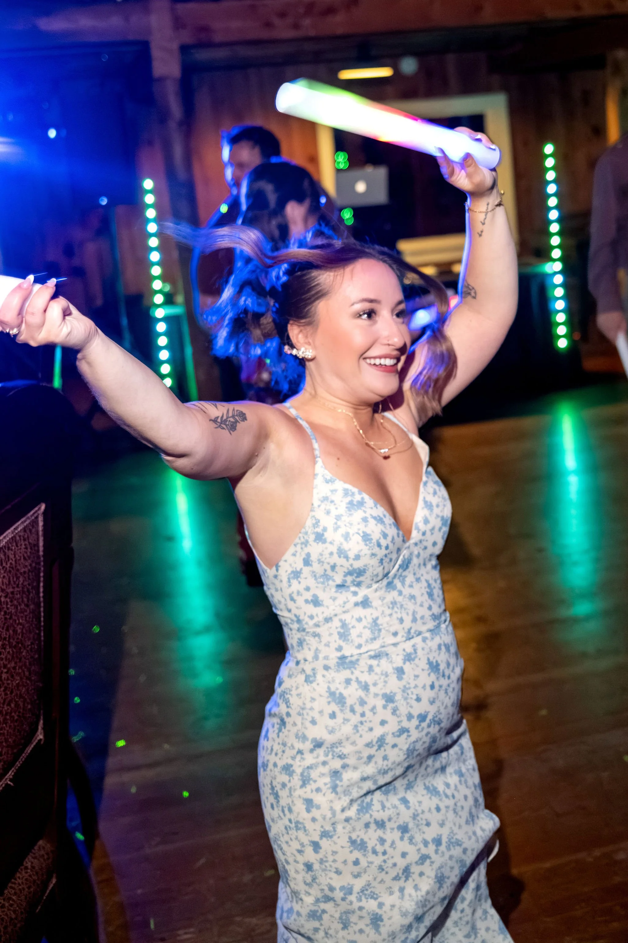The maid of honor dancing with a glow stick held high under blue and green lights at Boothbay Playhouse in Boothbay Maine fall wedding photography VMG Productions