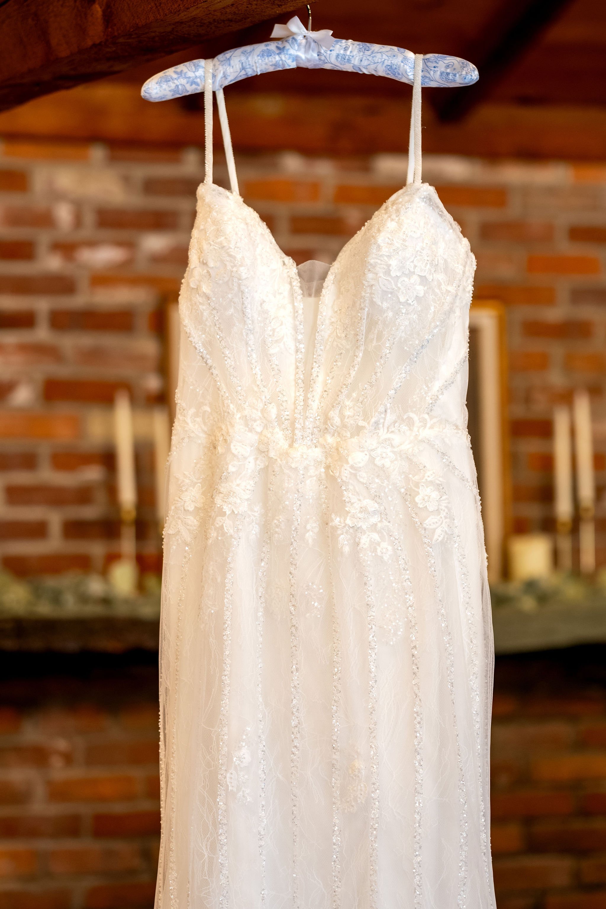 Ellie's lace wedding gown hanging from a hanger in front of an old brick wall at Boothbay Playhouse in Boothbay Maine fall wedding photography VMG Productions