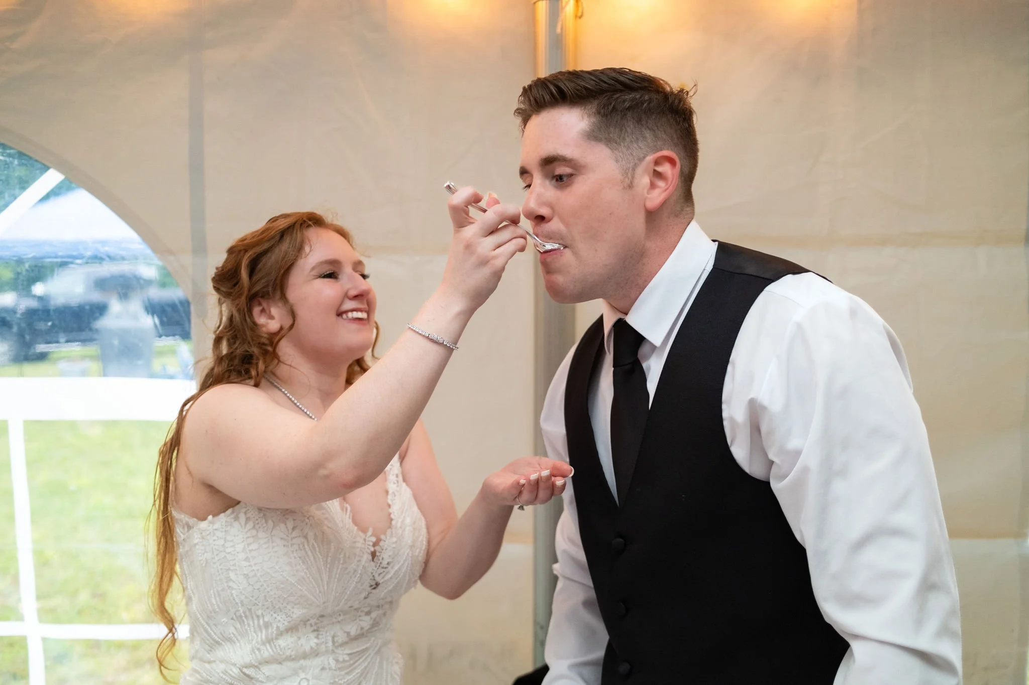 Kayla and Ethan DeAngelis cake feeding moment inside the reception tent at their Sanbornton New Hampshire wedding photography VMG Productions