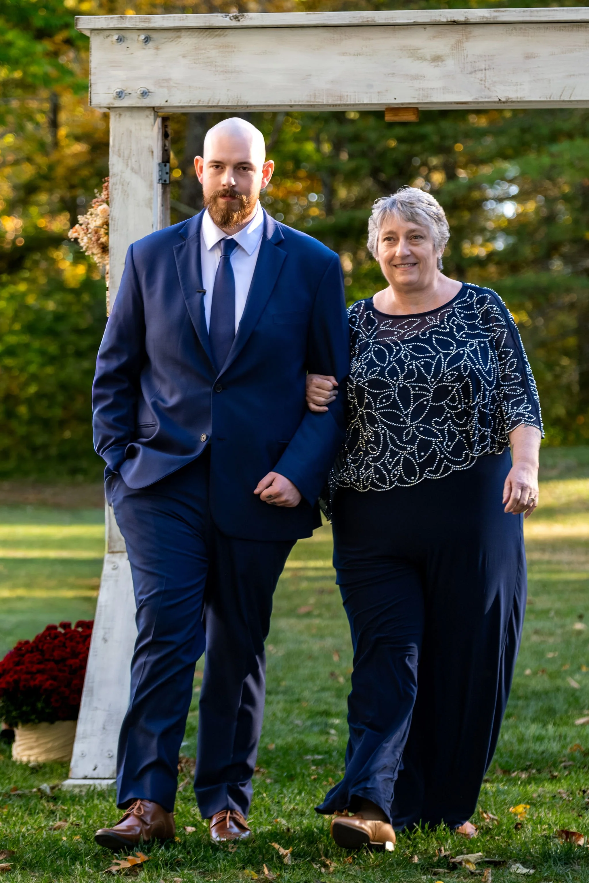 Sam walking down the aisle arm in arm with his mom under the pergola at Boothbay Playhouse in Boothbay Maine fall wedding photography VMG Productions