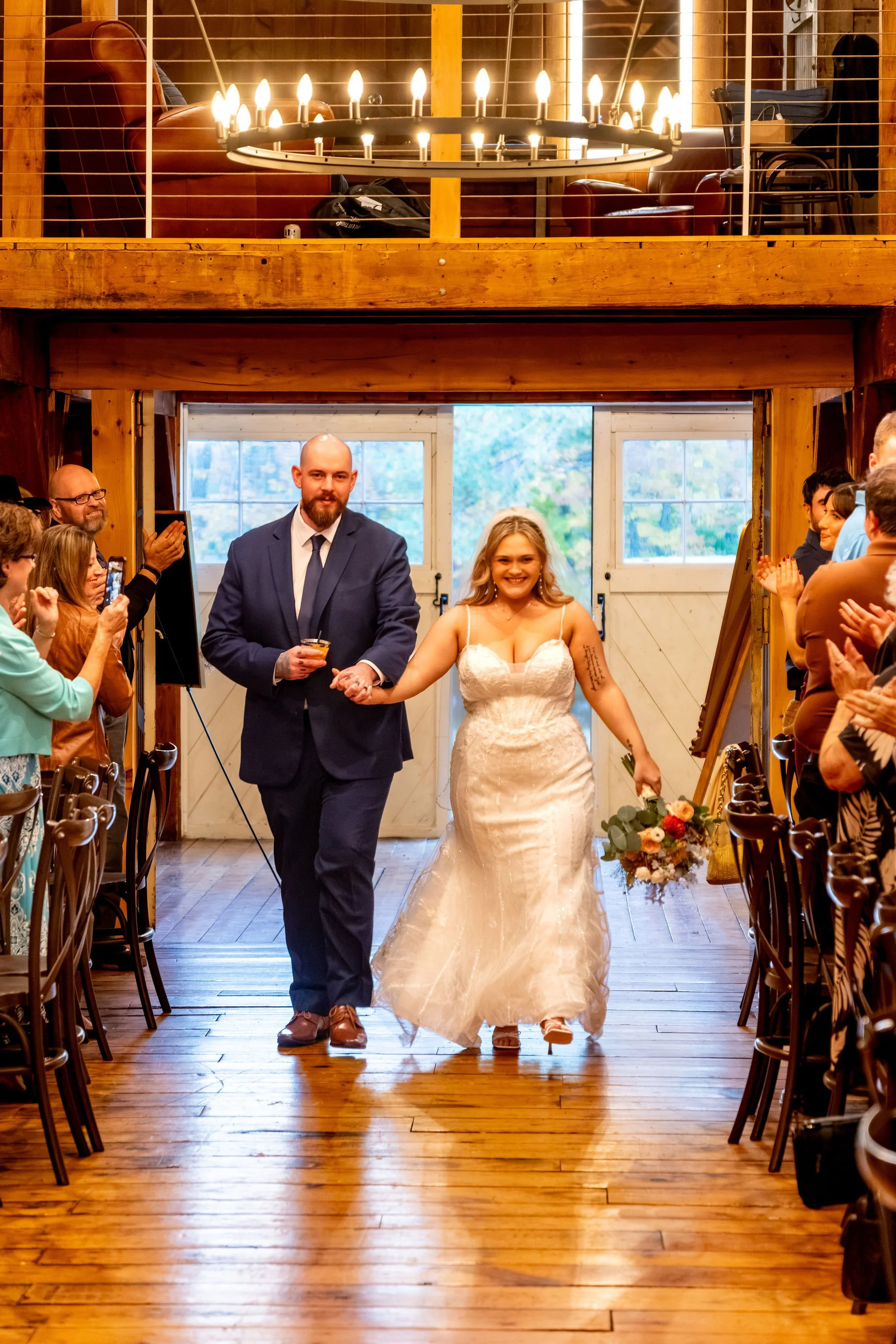 Ellie and Sam walking hand in hand into the barn as guests clap on both sides at Boothbay Playhouse in Boothbay Maine fall wedding photography VMG Productions