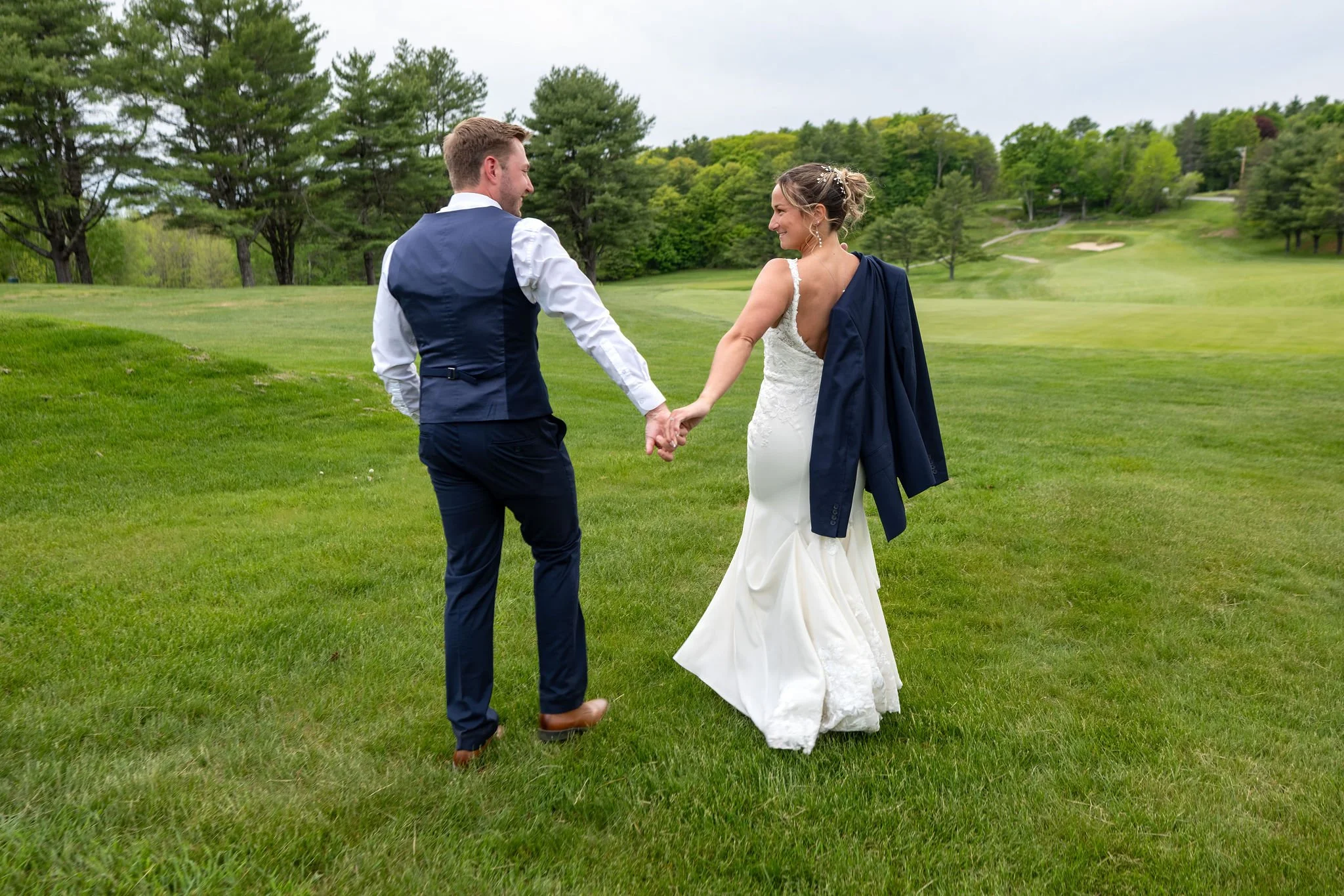 Beth and Cameron walking hand in hand across the golf course at Augusta Country Club Manchester Maine spring wedding photography VMG Productions