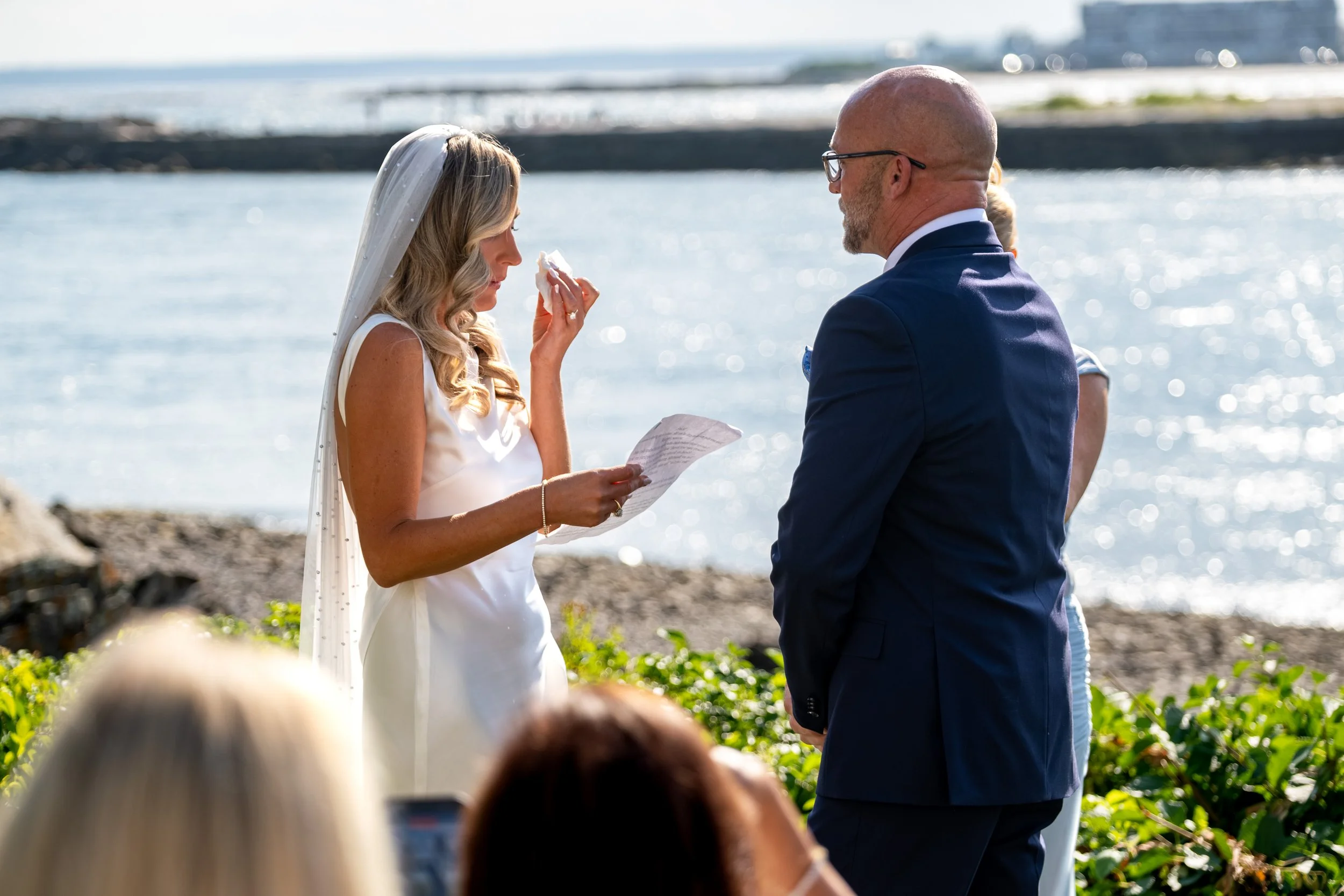 Ashley Draper wiping away a tear while reading her personal vows to Marc overlooking the water at The Breakwater Inn in Kennebunkport Maine summer wedding photography VMG Productions
