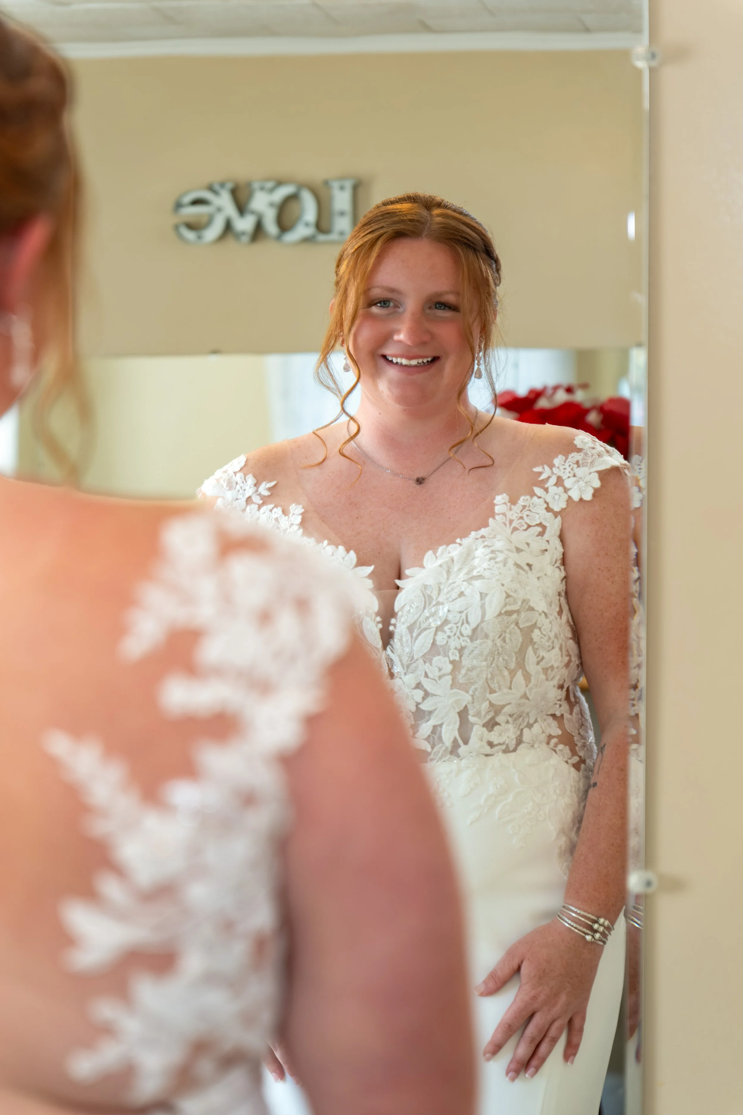Erika smiling at her reflection in a mirror with a HOME sign above it at the Maine Wedding Barn and Event Center in Minot Maine fall wedding photography VMG Productions