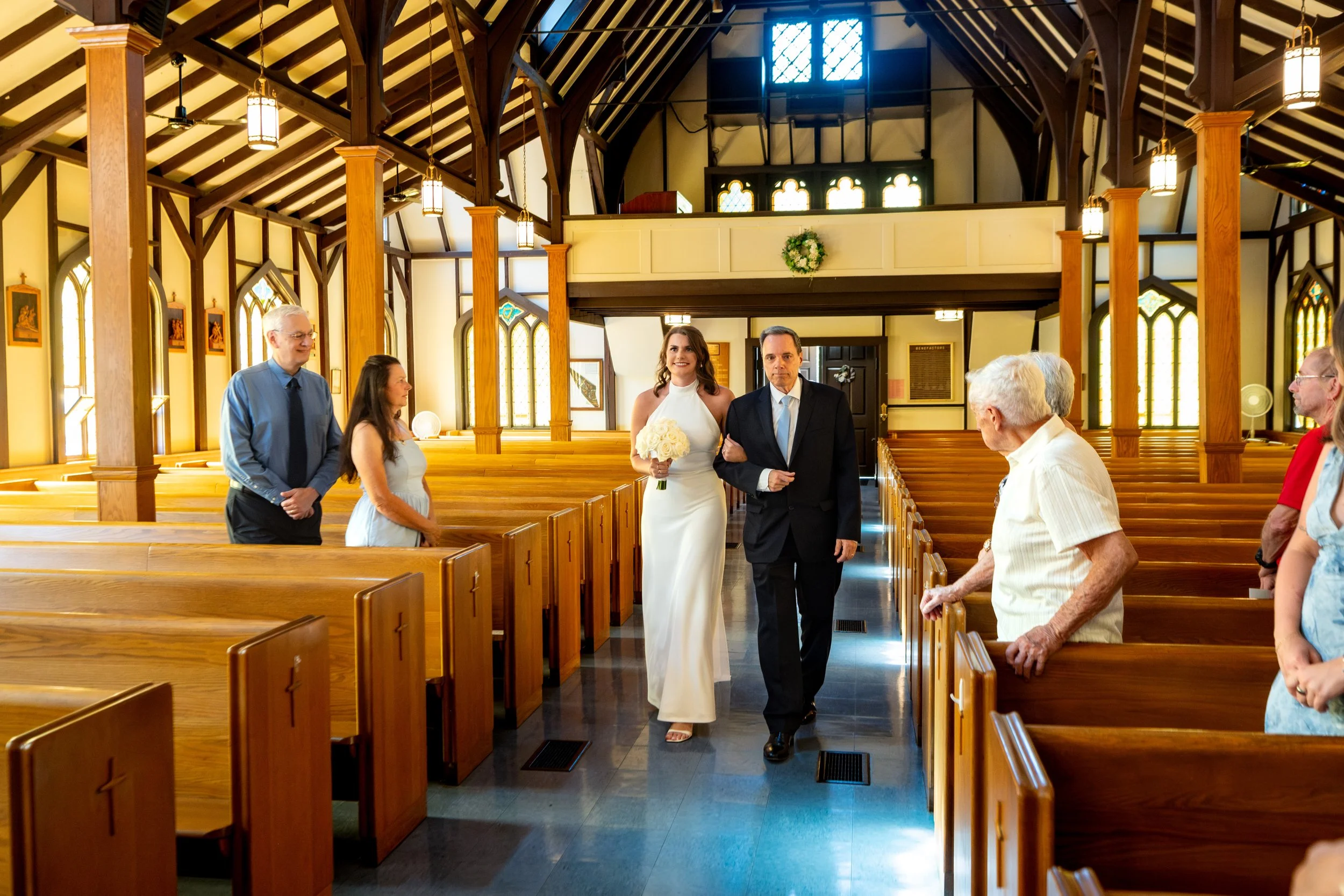 Caroline Joncas walking down the aisle on her father's arm beneath the timber-frame ceiling at Star of the Sea Catholic Church in York Maine wedding photography VMG Productions
