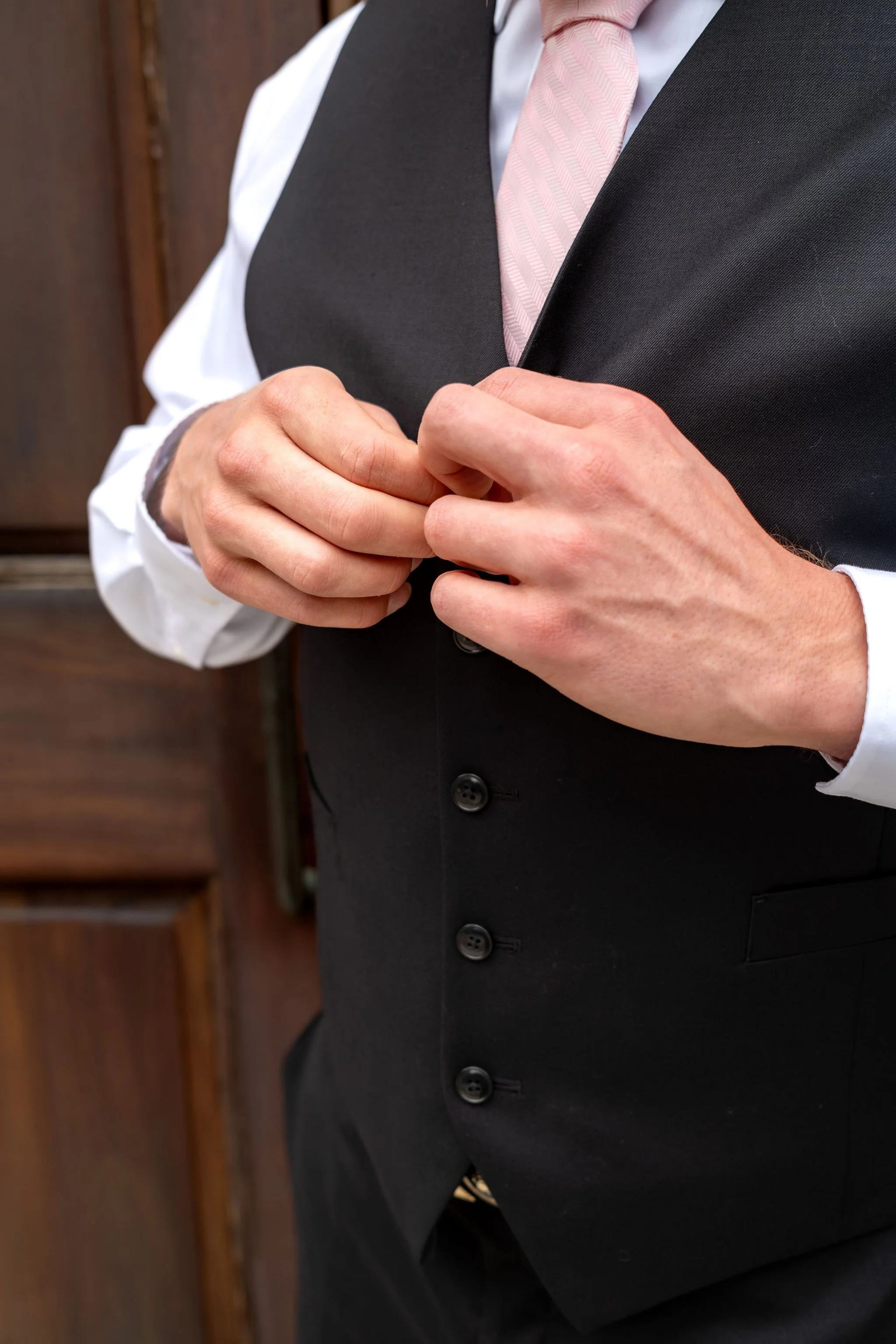 Jeremiah and Vienna tight crop showing groom buttoning vest before ceremony at Holy Trinity Greek Orthodox Church Portland Maine spring wedding photography VMG Productions