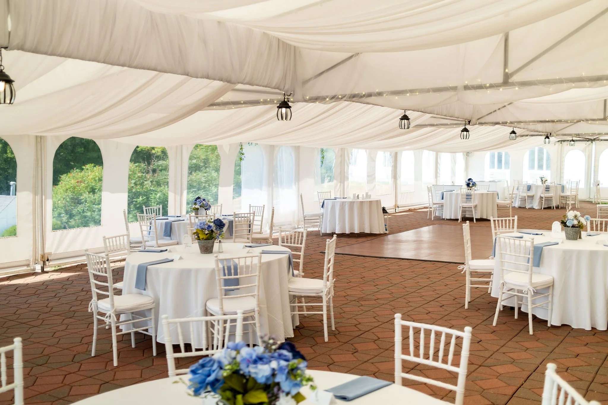 Wide view of the white reception tent set with round tables and blue linens before guests arrive at The Lucerne Inn in Dedham Maine summer wedding photography VMG Productions