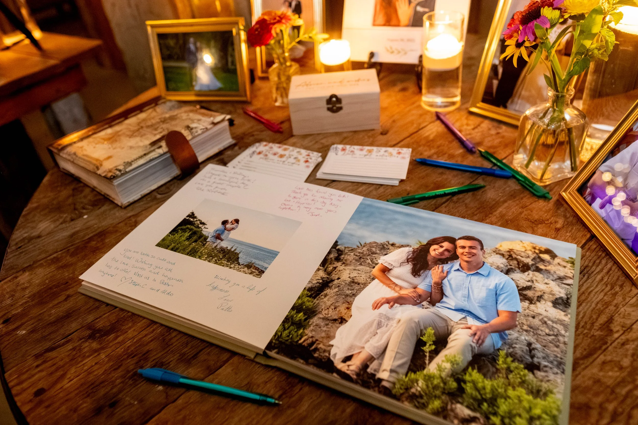 Open printed engagement photo album guest book at Mountain Star Estate Rangeley Maine barn wedding showing couple coastal portraits with white space filled with colorful handwritten guest messages and advice cards stacked alongside