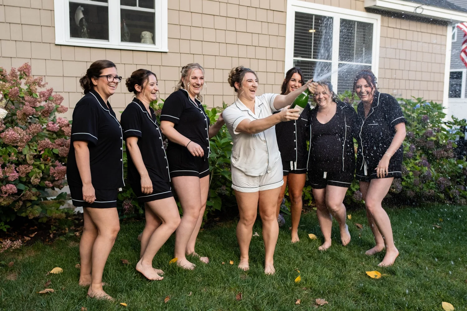 Bride spraying champagne with bridesmaids in matching pajamas during wedding morning getting ready at Union Bluff Meeting House York Maine