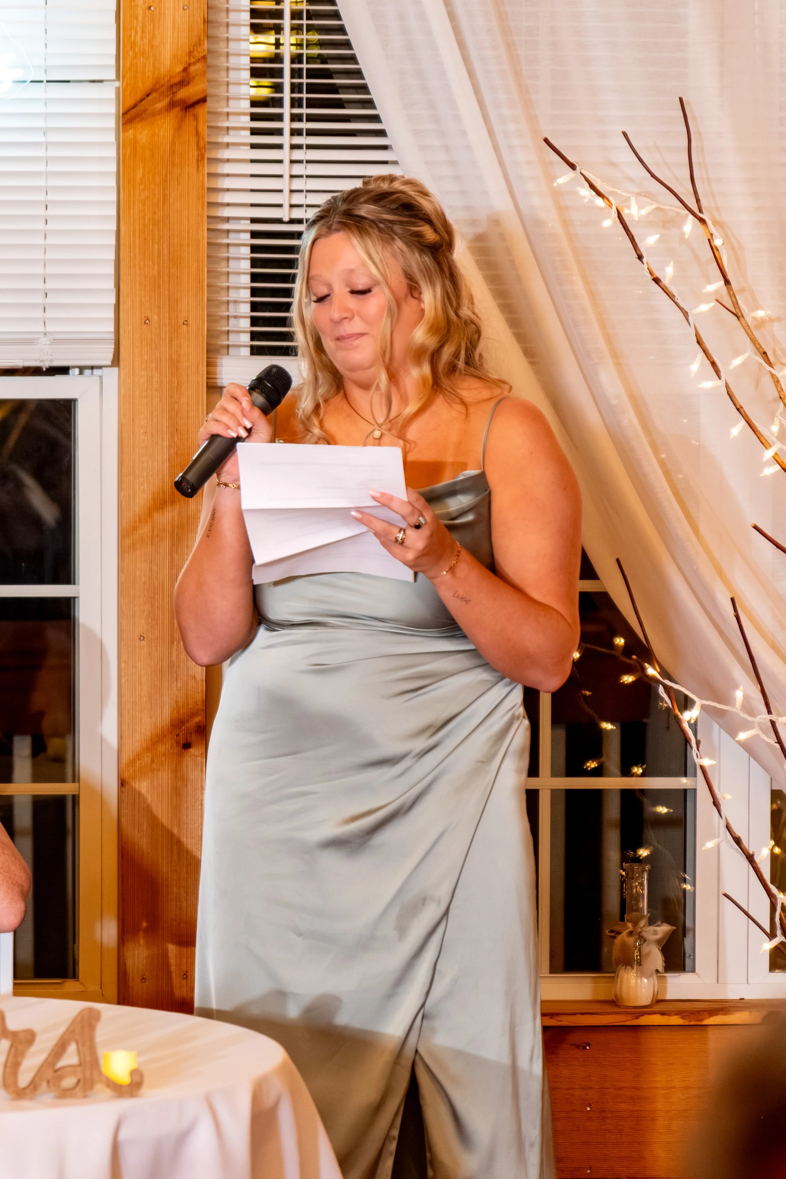 Erika's sister, the maid of honor, in a sage dress reading her toast into the microphone at the Maine Wedding Barn and Event Center in Minot Maine fall wedding photography VMG Productions