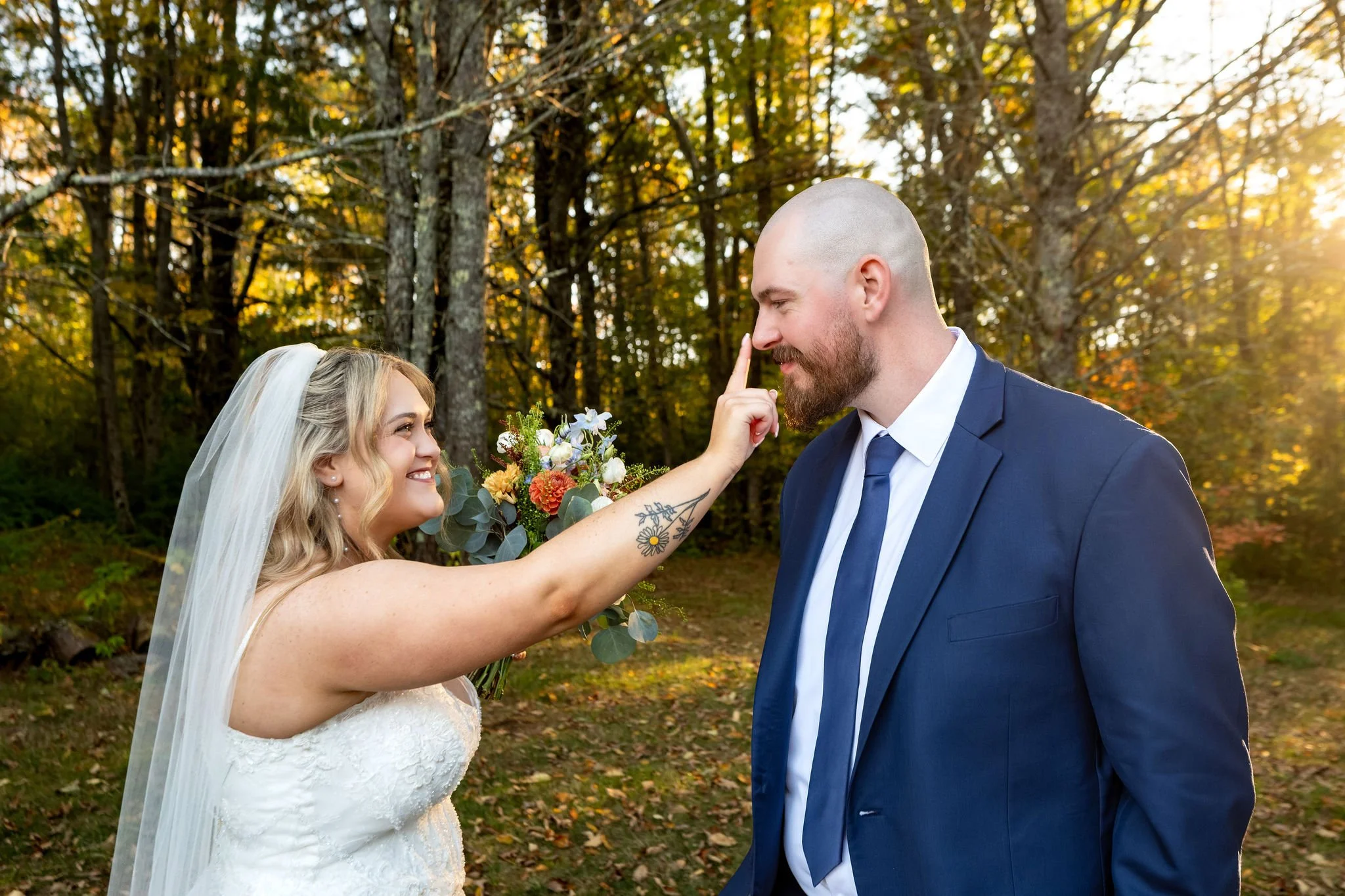 Ellie playfully touching Sam's nose as he smiles down at her in the golden light at Boothbay Playhouse in Boothbay Maine fall wedding photography VMG Productions