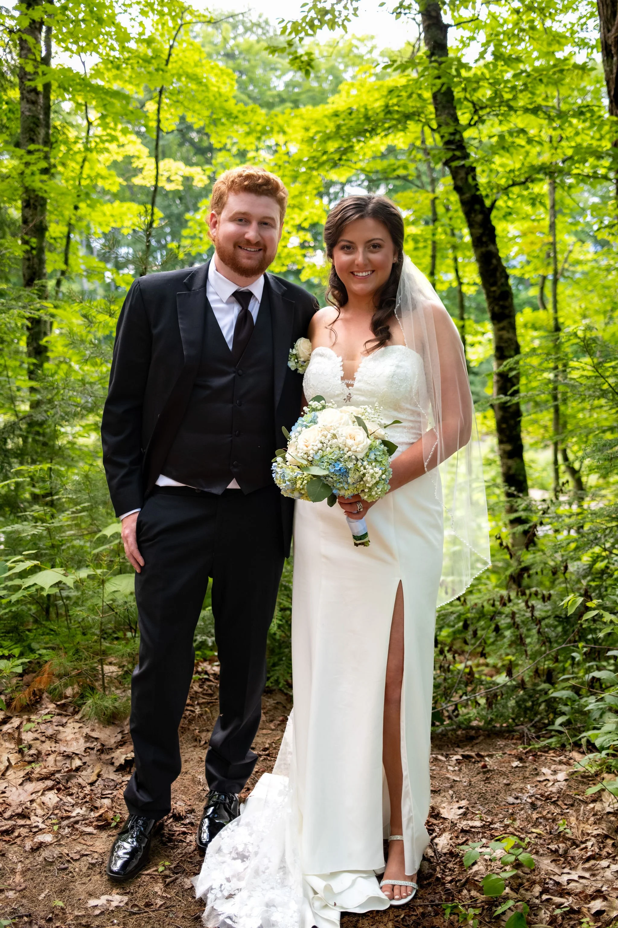 Alyssa and Colby standing together in the summer forest near the river at Sunday River Covered Bridge Newry Maine summer wedding photography VMG Productions