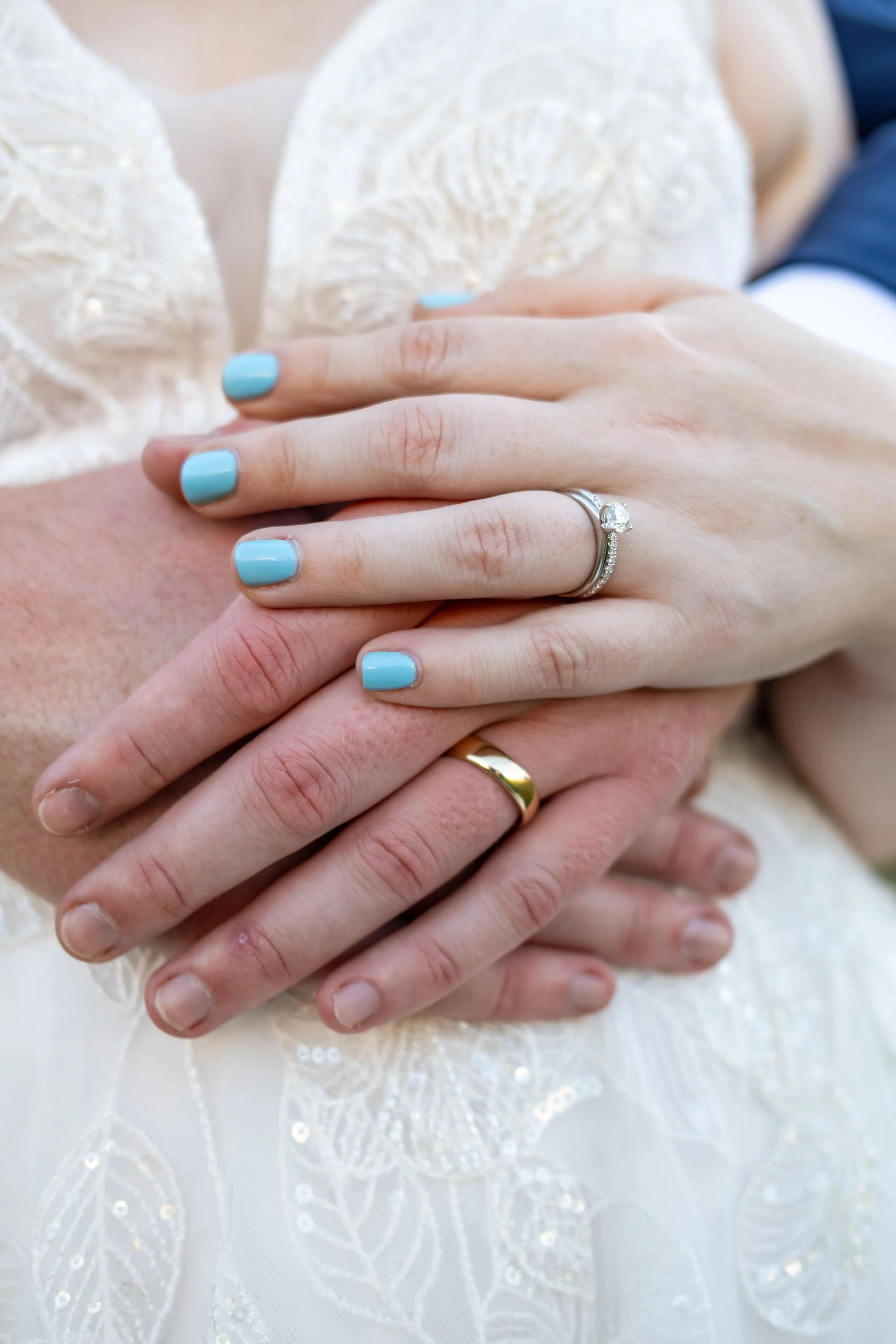 Close detail of Zachary and Hollie's wedding rings with her blue nails as his arms wrap around her waist at The Lucerne Inn in Dedham Maine summer wedding photography VMG Productions