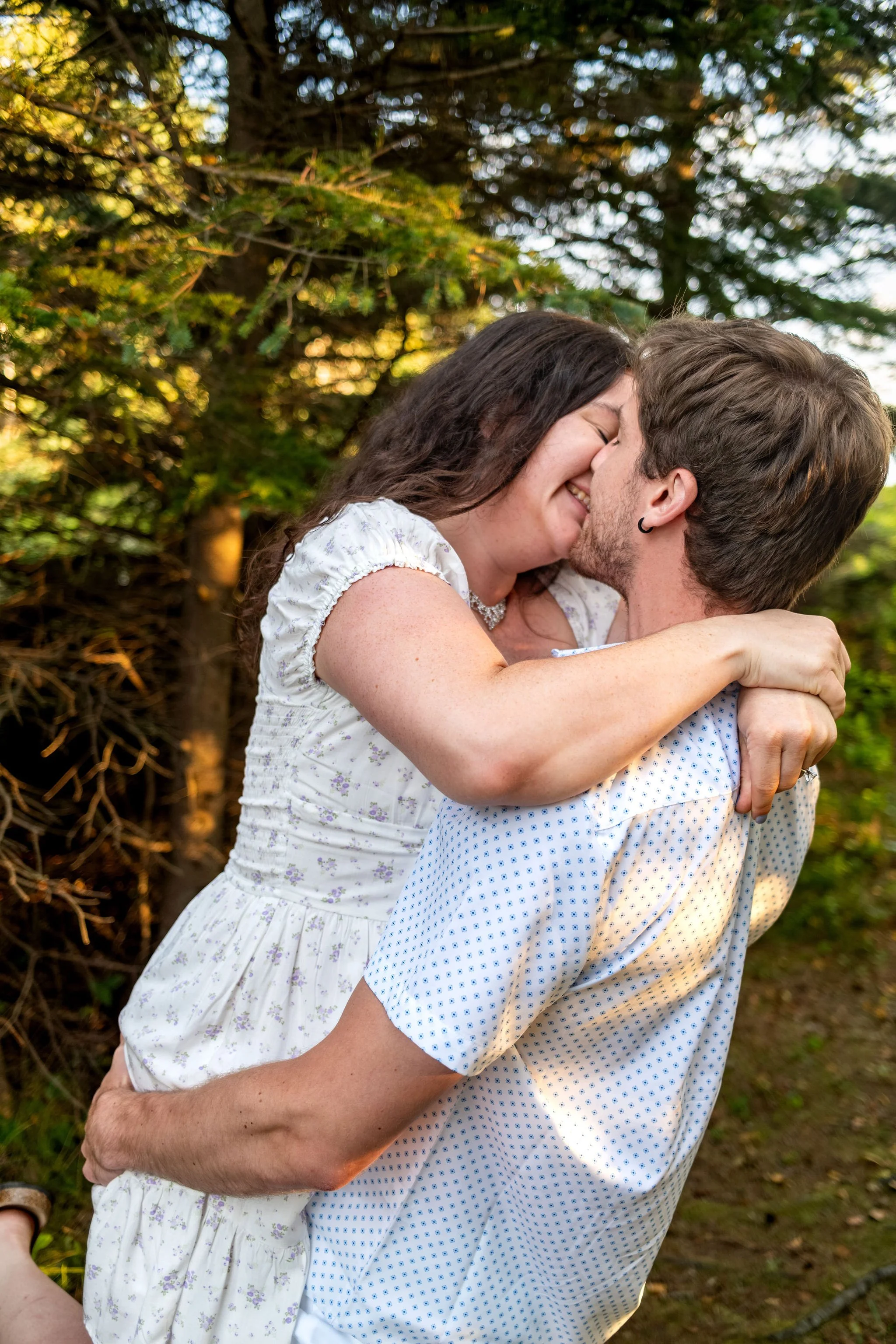 Lucas lifting Kirstie off the ground for a kiss in the golden light under the trees at Reid State Park in Georgetown Maine engagement photography VMG Productions