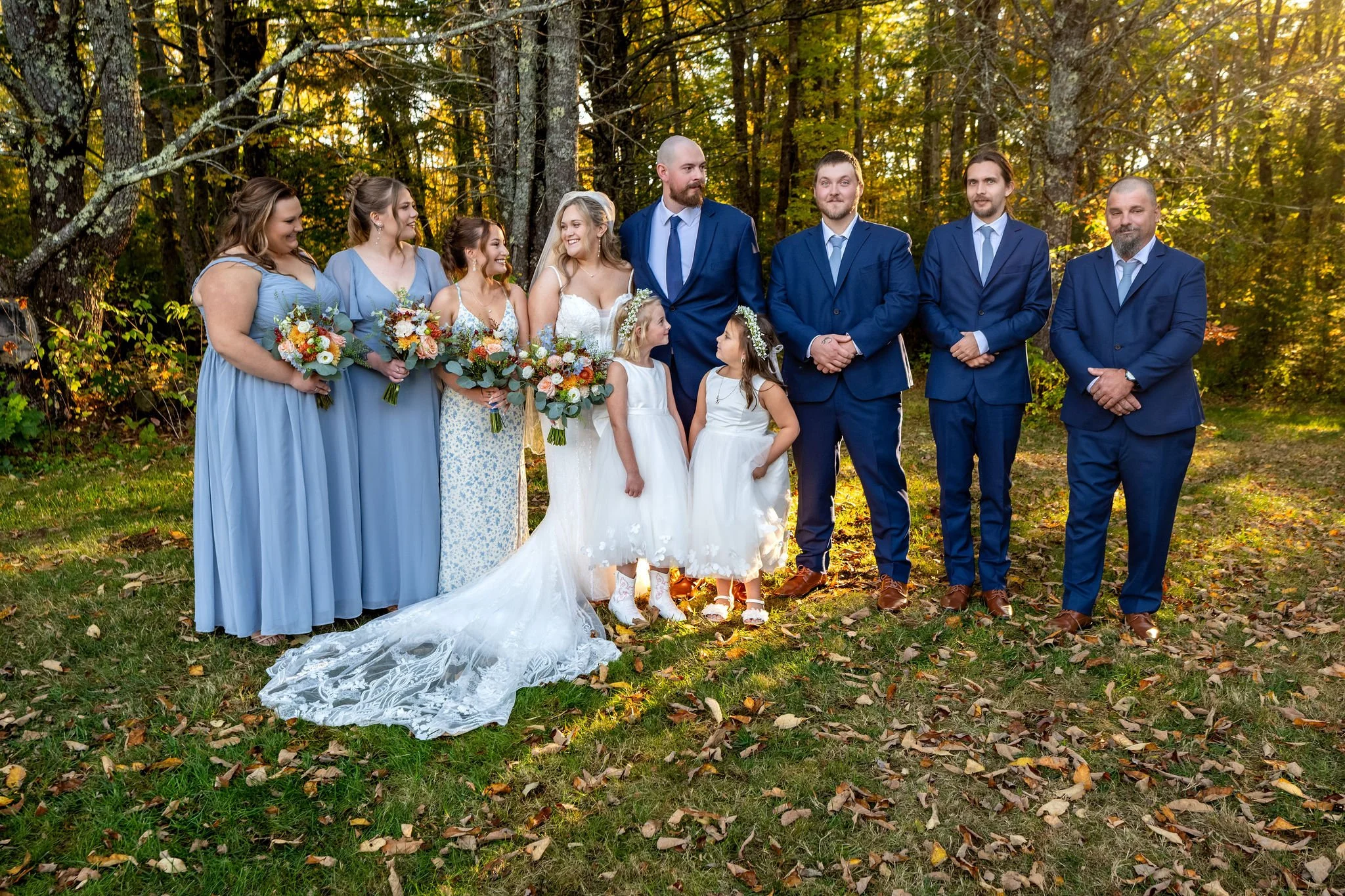 Ellie and Sam with the wedding party and two flower girls lined up in the golden light under the trees at Boothbay Playhouse in Boothbay Maine fall wedding photography VMG Productions