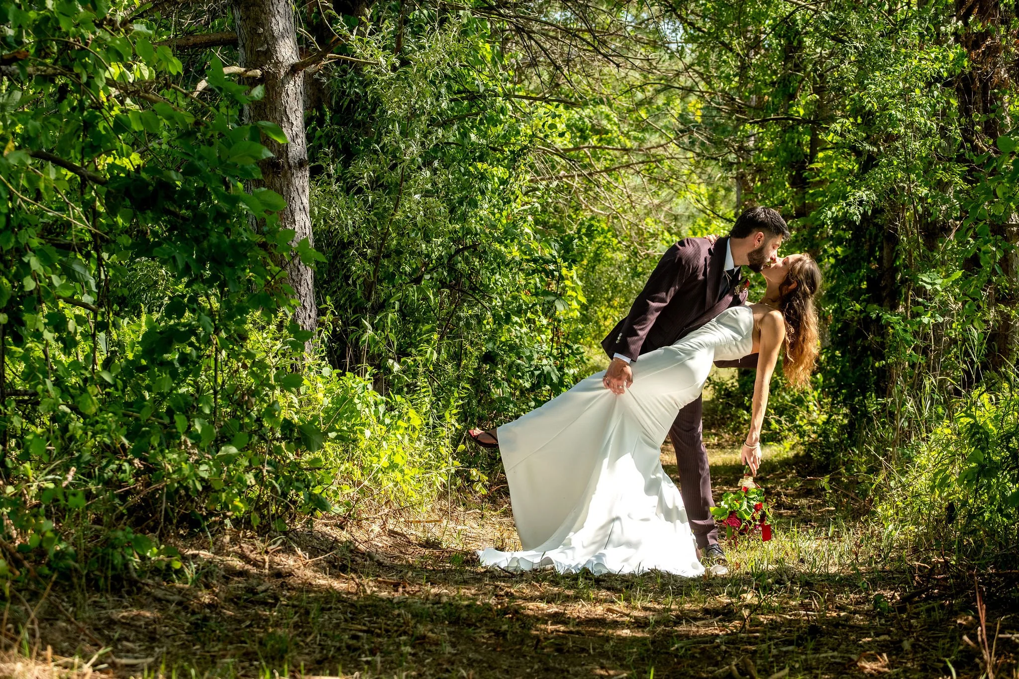 Chase Begin dipping Cassidy for a kiss on a sunlit pine trail at Maple Hill Farm Inn and Conference Center in Hallowell Maine summer wedding photography VMG Productions