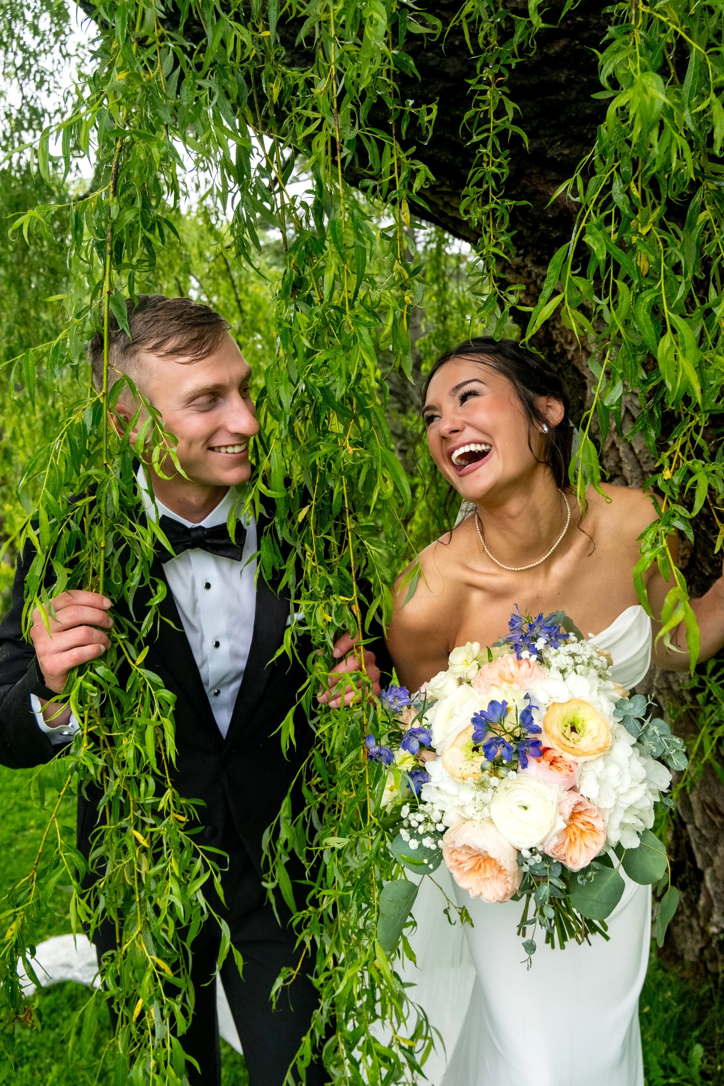 Bride and groom laughing together under a weeping willow at a Maine wedding