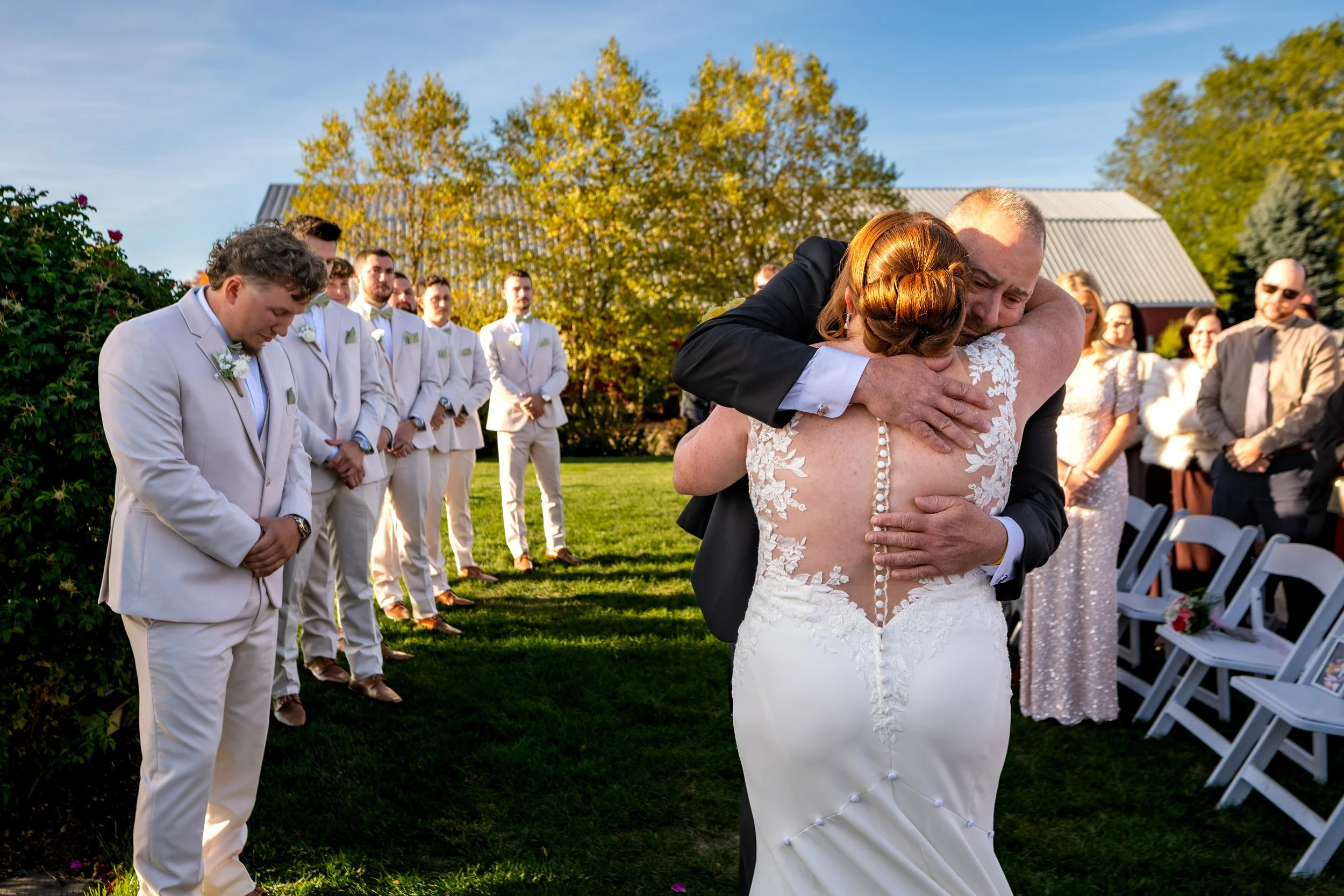 Erika hugging her dad at the front of the aisle as Andrew's groomsmen look on at the Maine Wedding Barn and Event Center in Minot Maine fall wedding photography VMG Productions