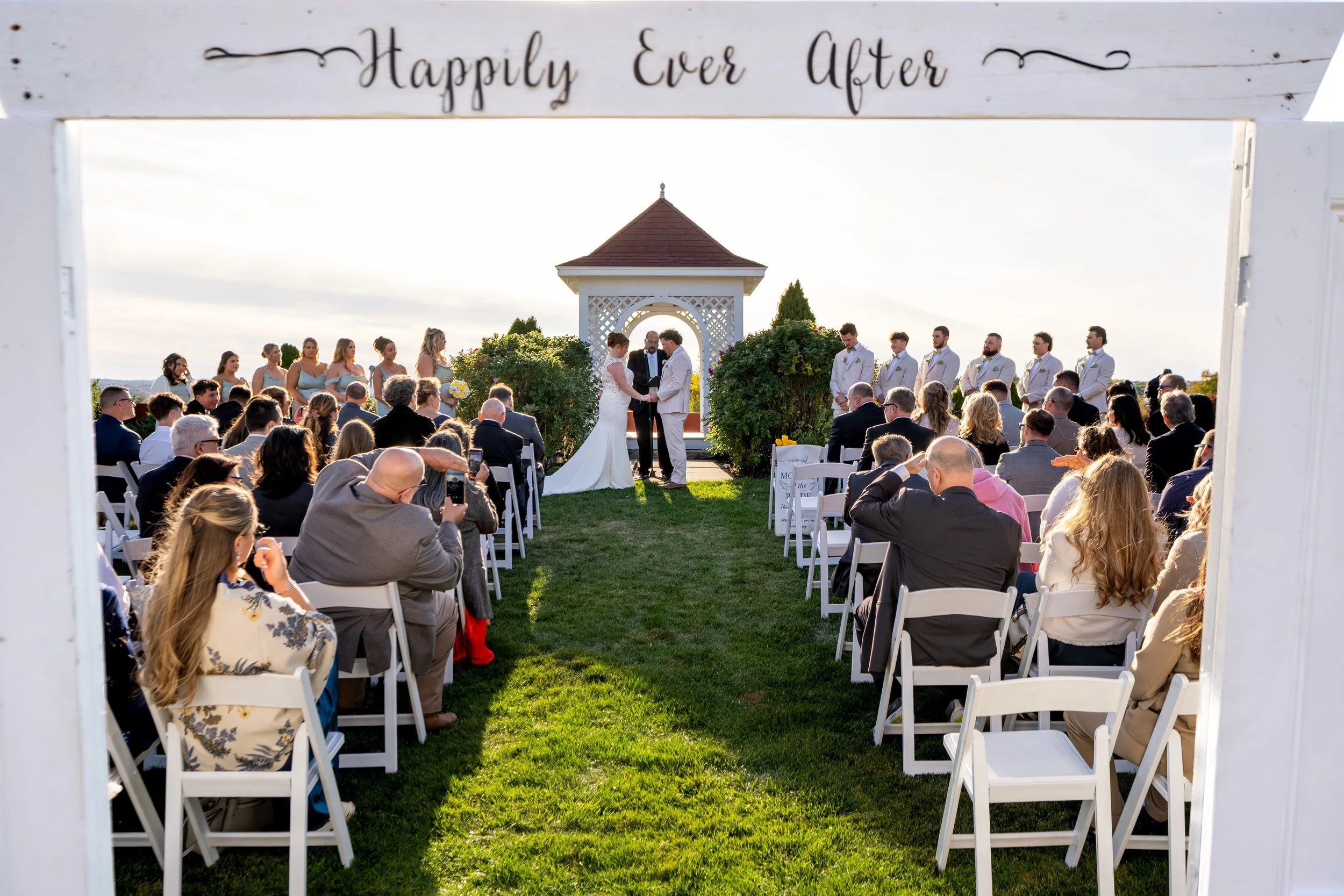 Wide view of the ceremony under the gazebo with guests seated along the lawn at the Maine Wedding Barn and Event Center in Minot Maine fall wedding photography VMG Productions